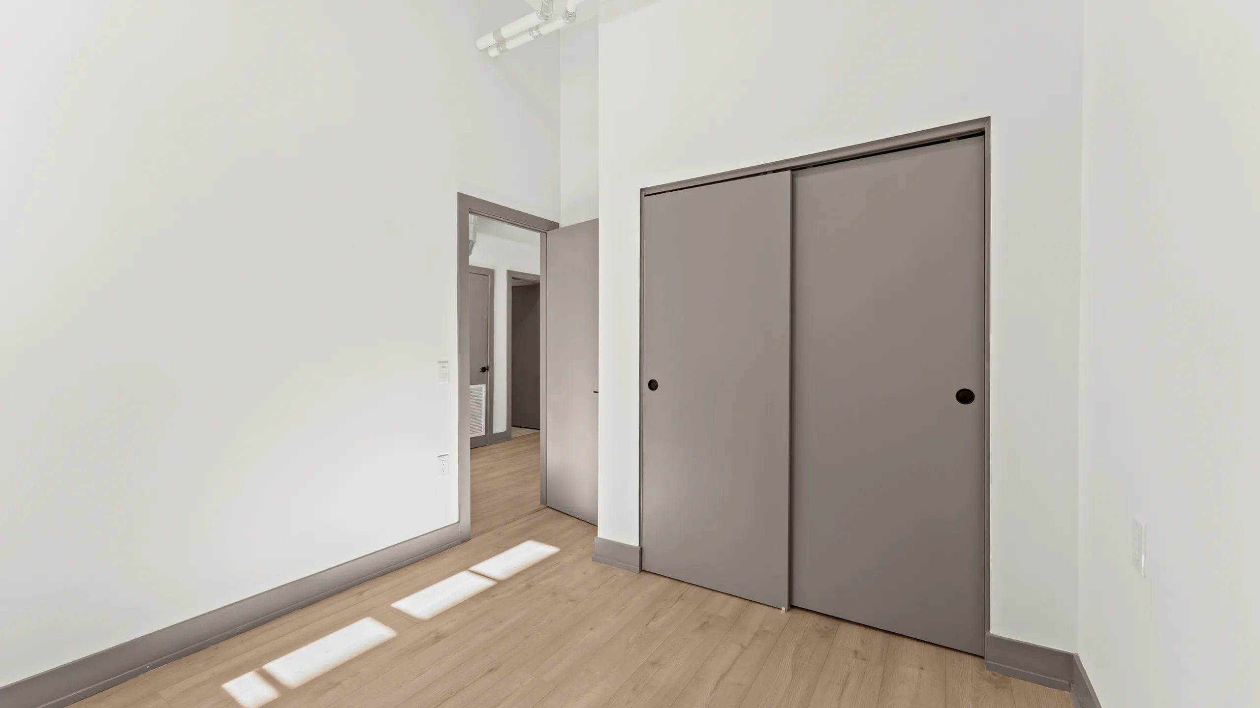 Bright minimalist room with light wood flooring and double sliding door closet, offering modern storage solutions.