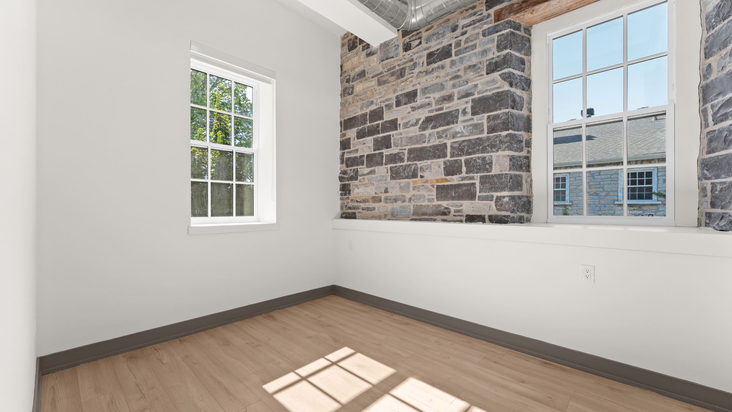 Bright and cozy room with a rustic stone accent wall, modern light wood flooring, and large sunlit windows.