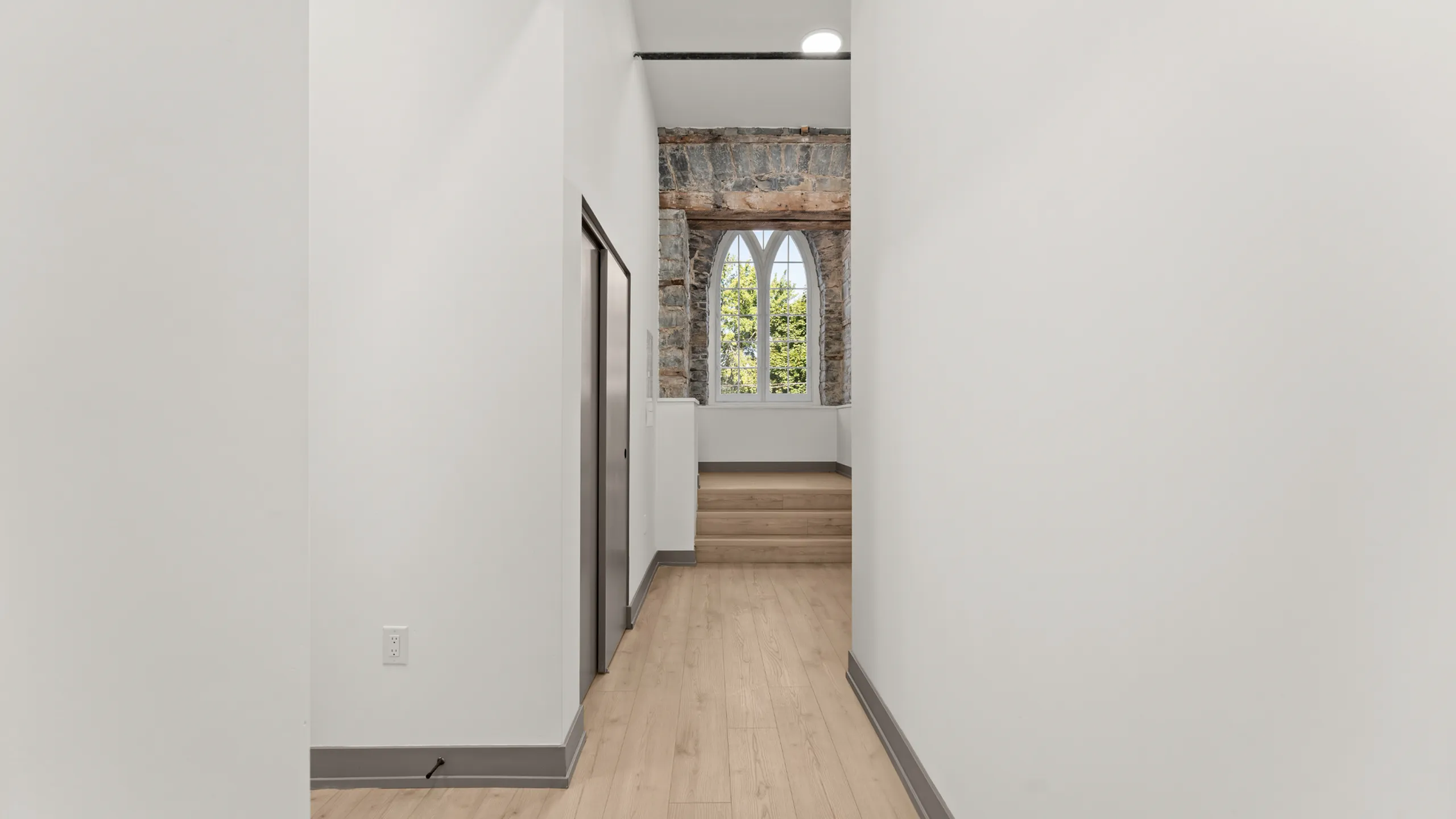 Bright and inviting hallway featuring elegant stonework and a classic arched window, leading up to a cozy, warmly lit space.