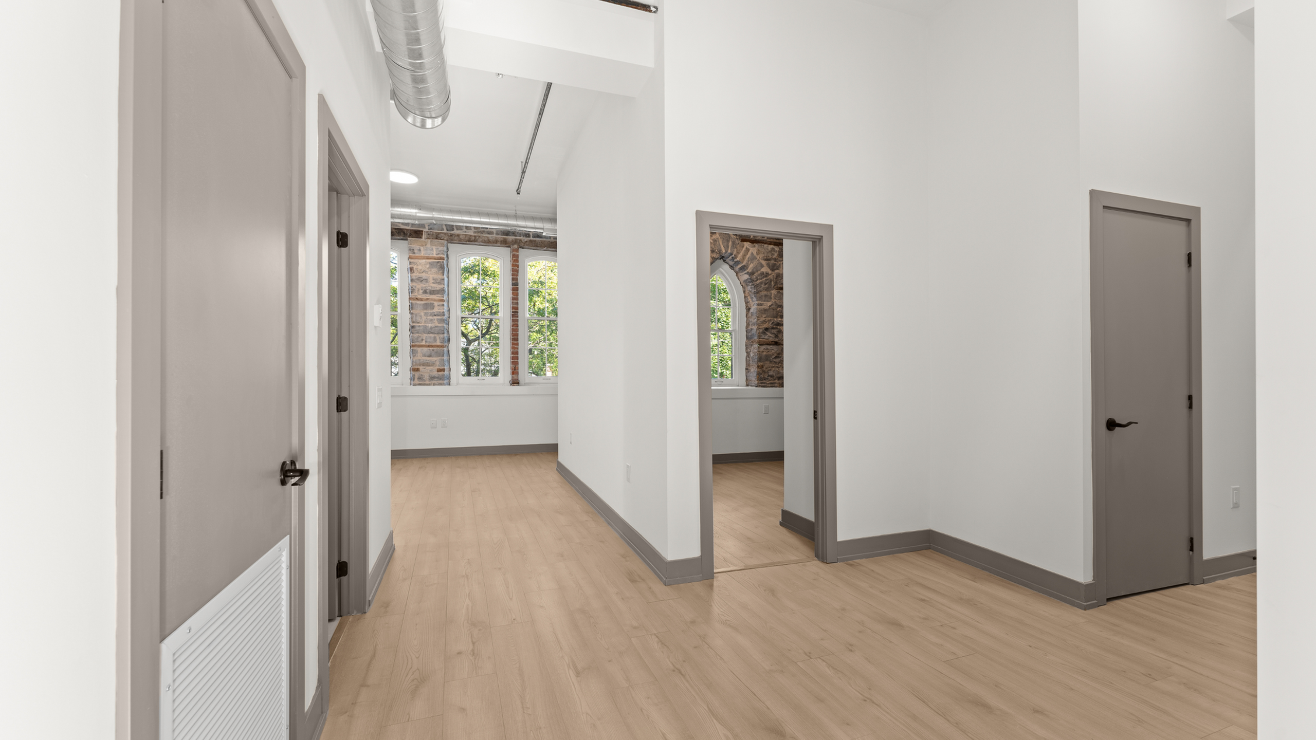 Bright and airy apartment entryway featuring contemporary doors, elegant wood flooring, and large arched windows with brick accents.