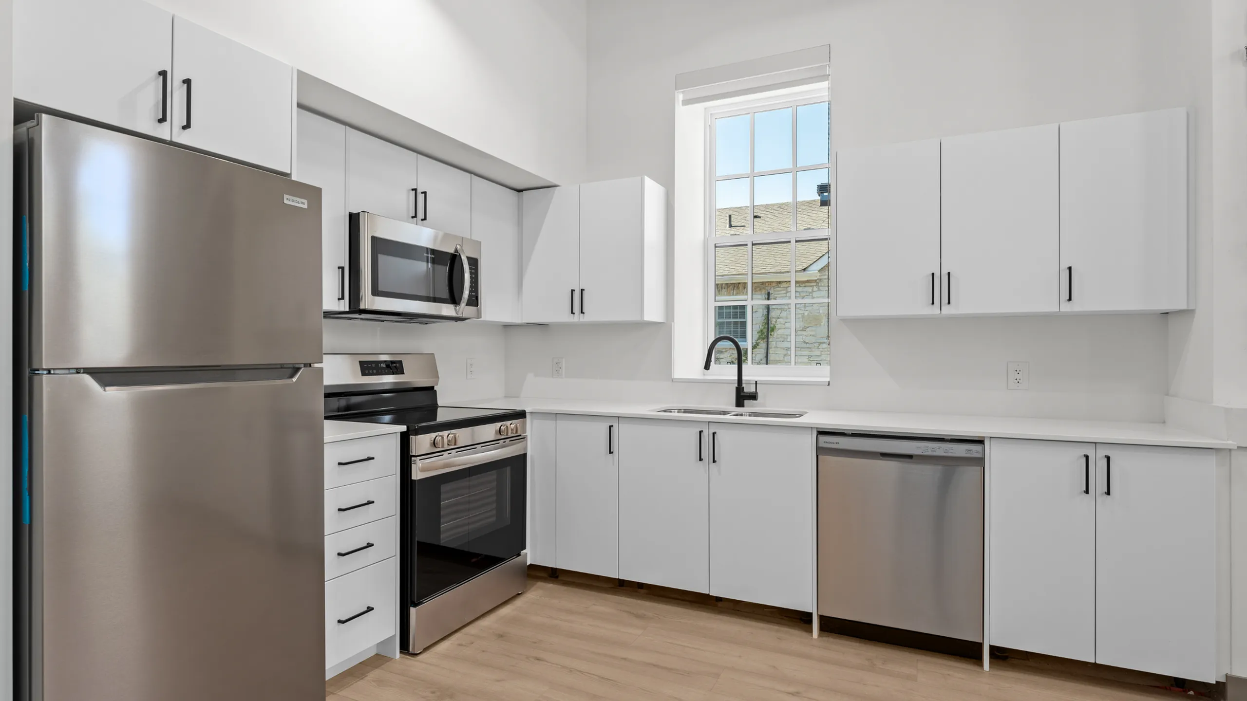 Modern kitchen with sleek stainless steel appliances, elegant cabinetry, and large window providing natural light.
