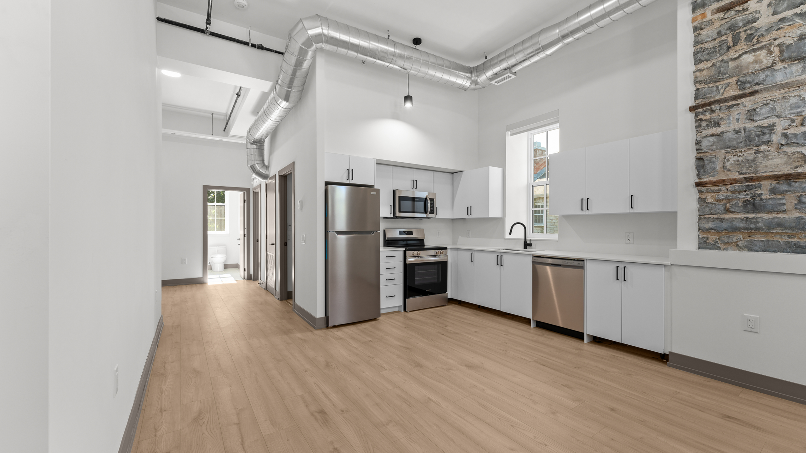 Modern apartment kitchen with sleek stainless steel appliances, bright cabinetry, and industrial exposed ductwork design.