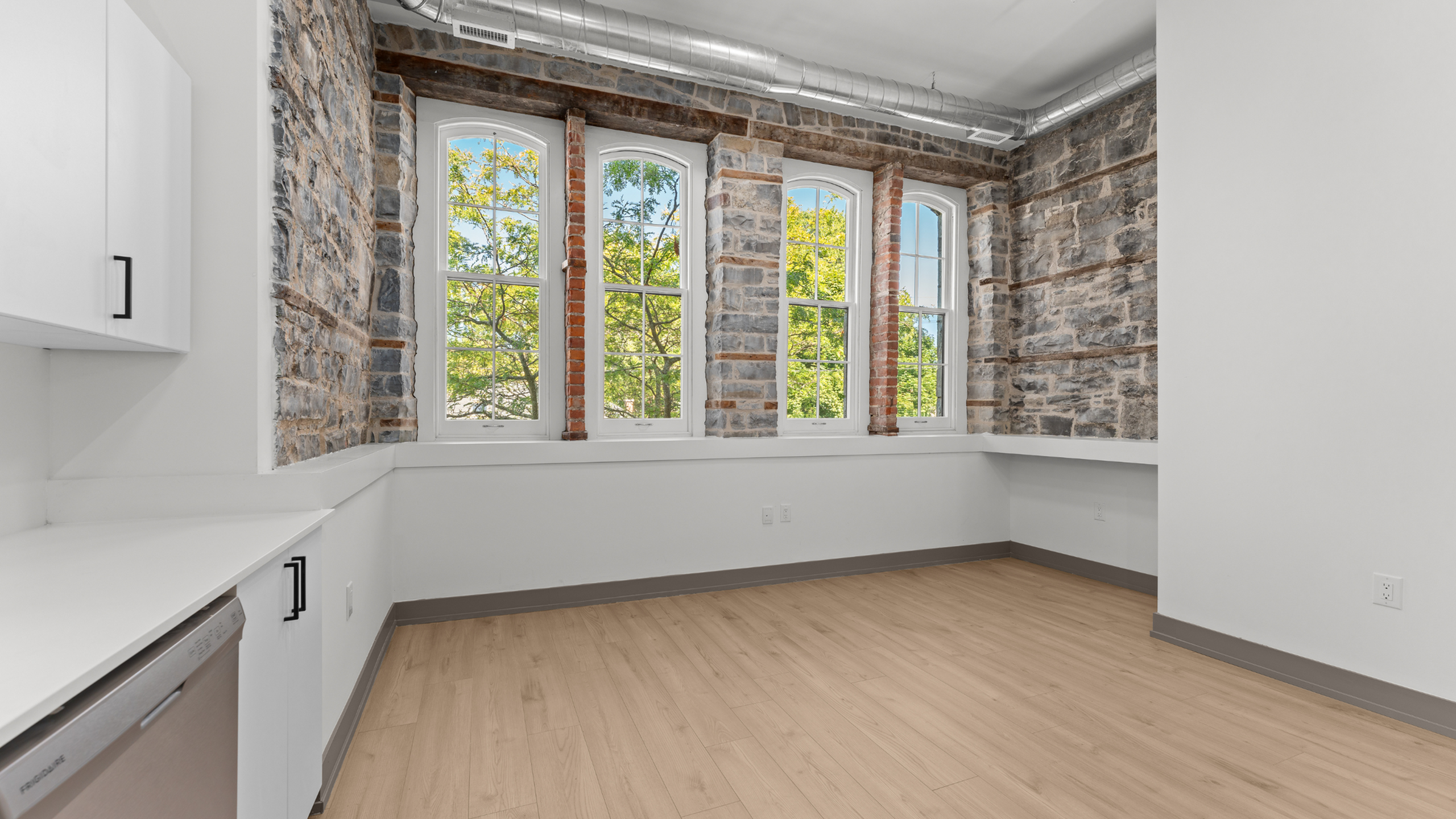 Charming room with exposed brick walls, large windows offering ample natural light, and sleek hardwood floors.