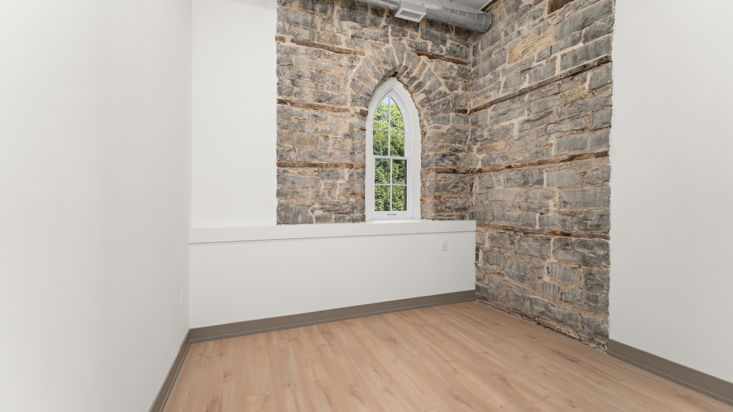 Charming room with rustic stone wall and arched window, offering a blend of contemporary and historic details.