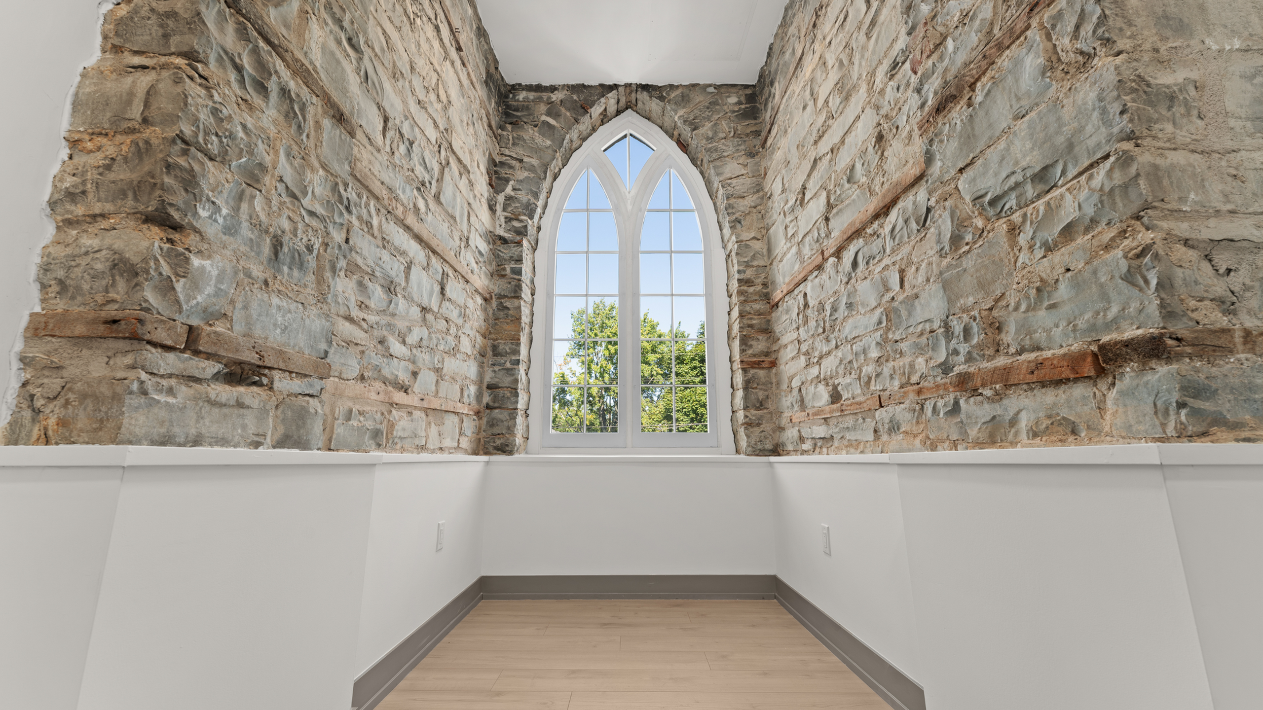 Charming interior featuring exposed stone walls and an elegant arched window with a scenic view.