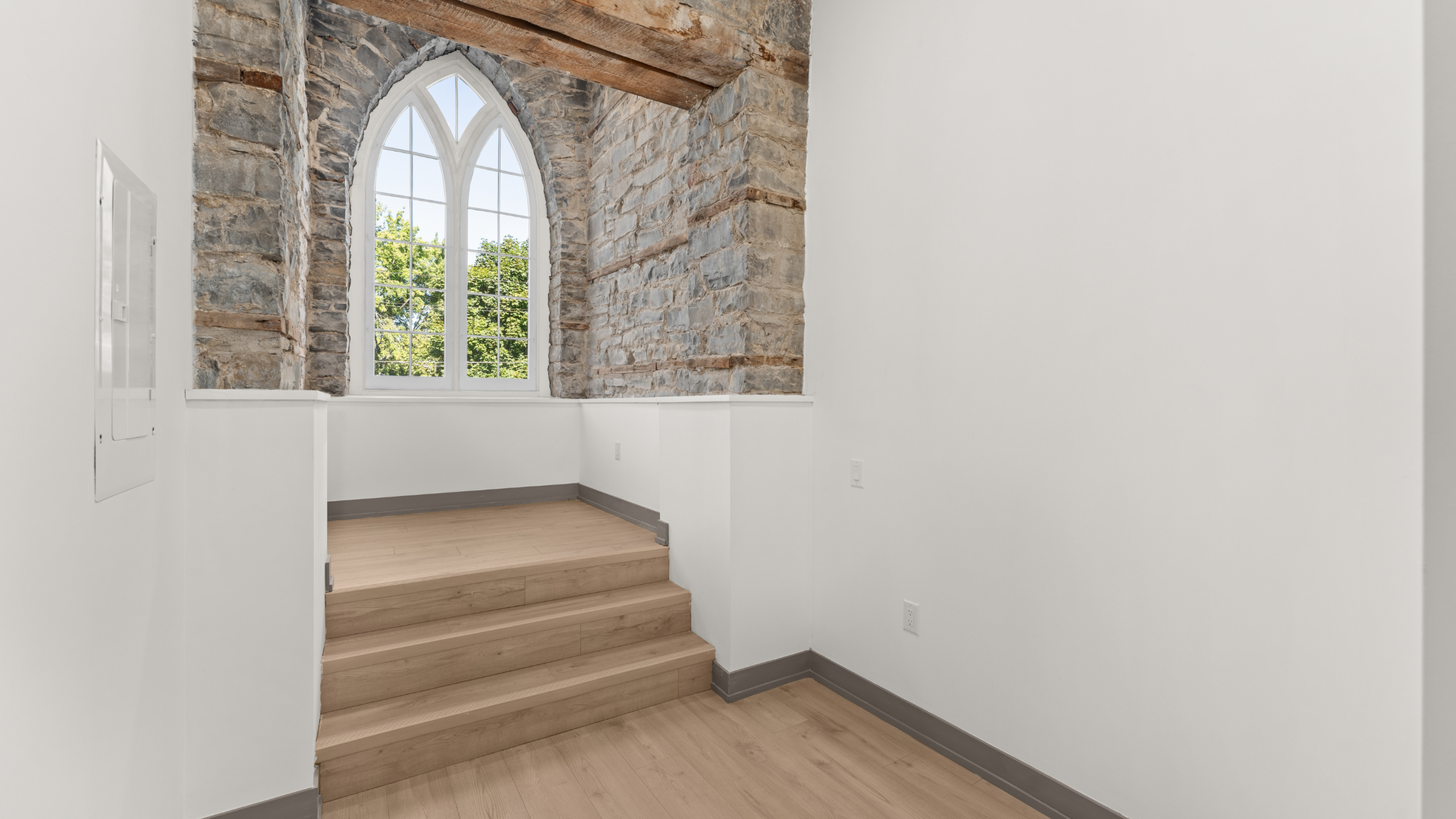 Charming room with arched stone window, rustic wooden beams, and bright natural light.