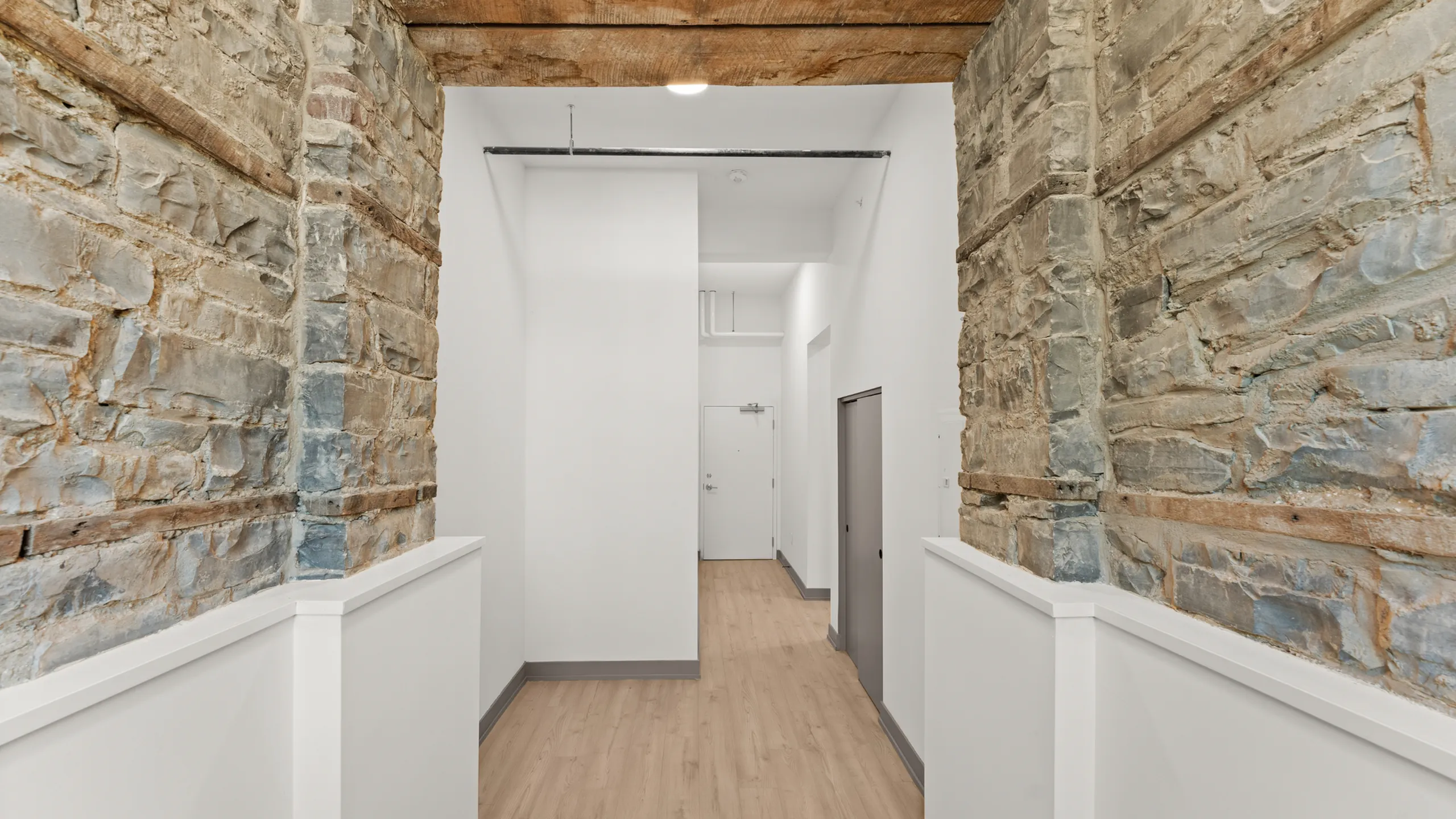 Charming hallway with rustic stone walls, clean white accents, and modern wood floors, creating a unique blend of historical and contemporary design.