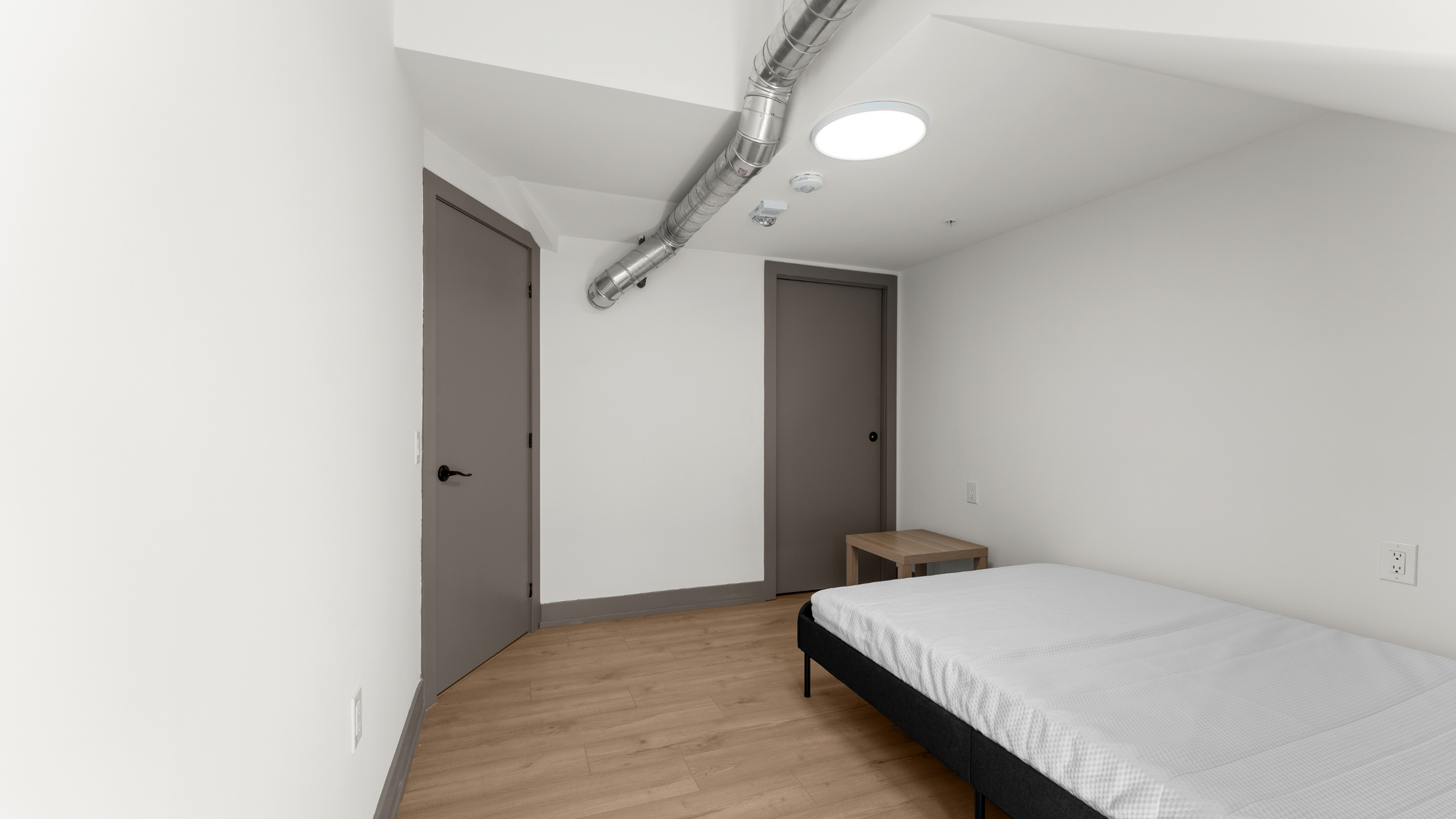 Modern bedroom with sleek minimalist design, featuring a cozy bed, stylish wood flooring, and contemporary lighting.