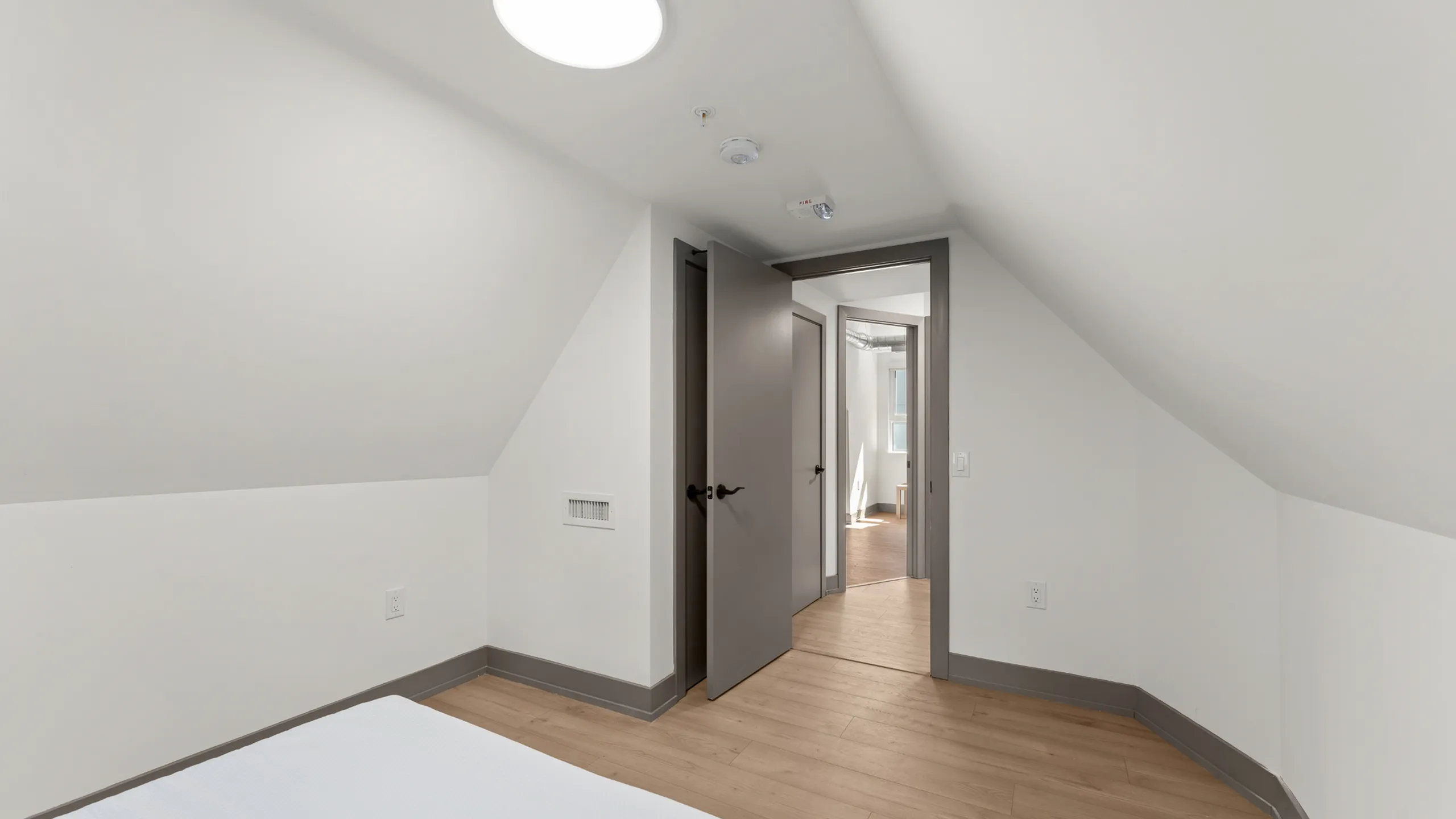 Bright attic bedroom with sloped ceiling and modern finishes, featuring light wood flooring and elegant doorway.