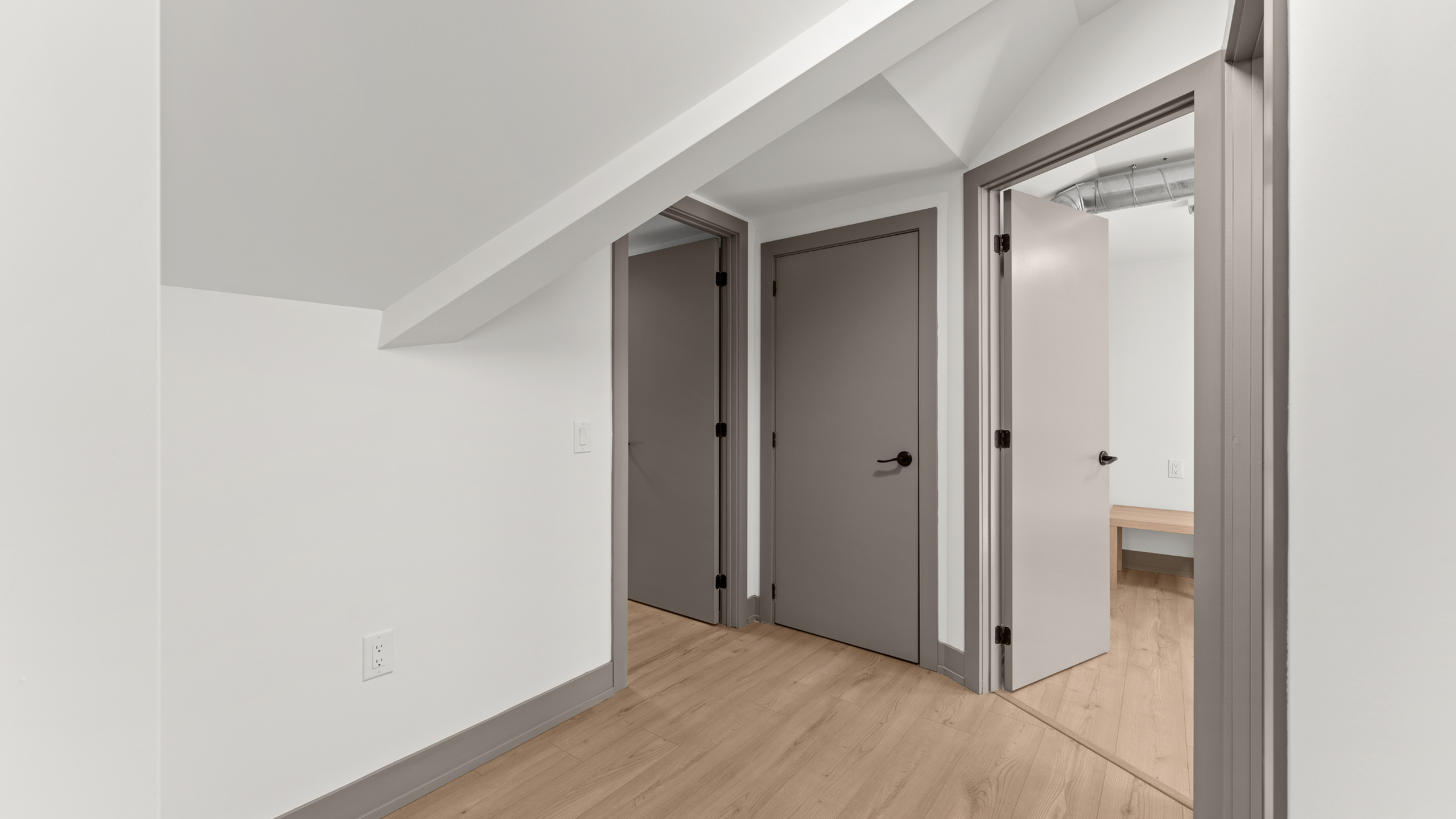 Modern apartment interior with sleek wooden flooring, crisp white walls, and three contemporary doors in a minimalist hallway.