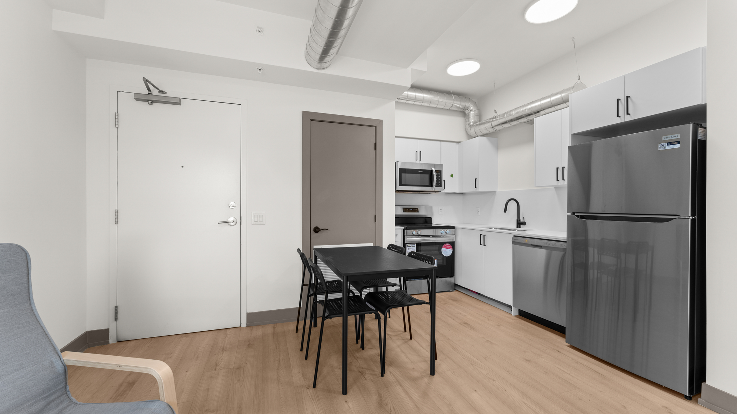 Modern kitchen and dining area with sleek appliances and minimalist decor, highlighted by a large stainless steel refrigerator and contemporary dining table.