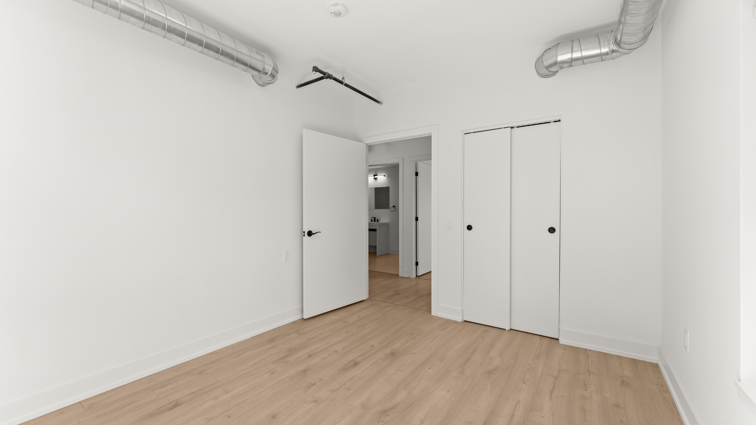 Chic and modern bedroom with sleek hardwood floors, pristine white walls, and stylish exposed ductwork, offering a minimalist and airy vibe.