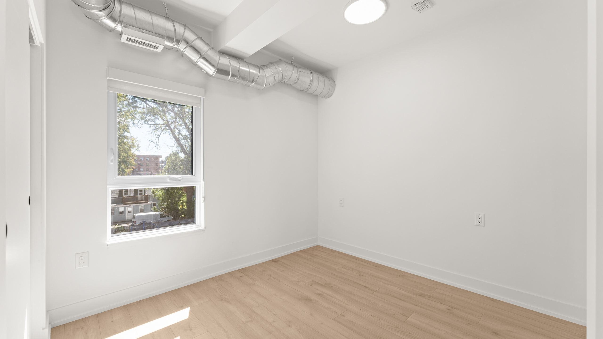Bright and airy room with sleek hardwood floors, large window, and modern exposed ductwork.
