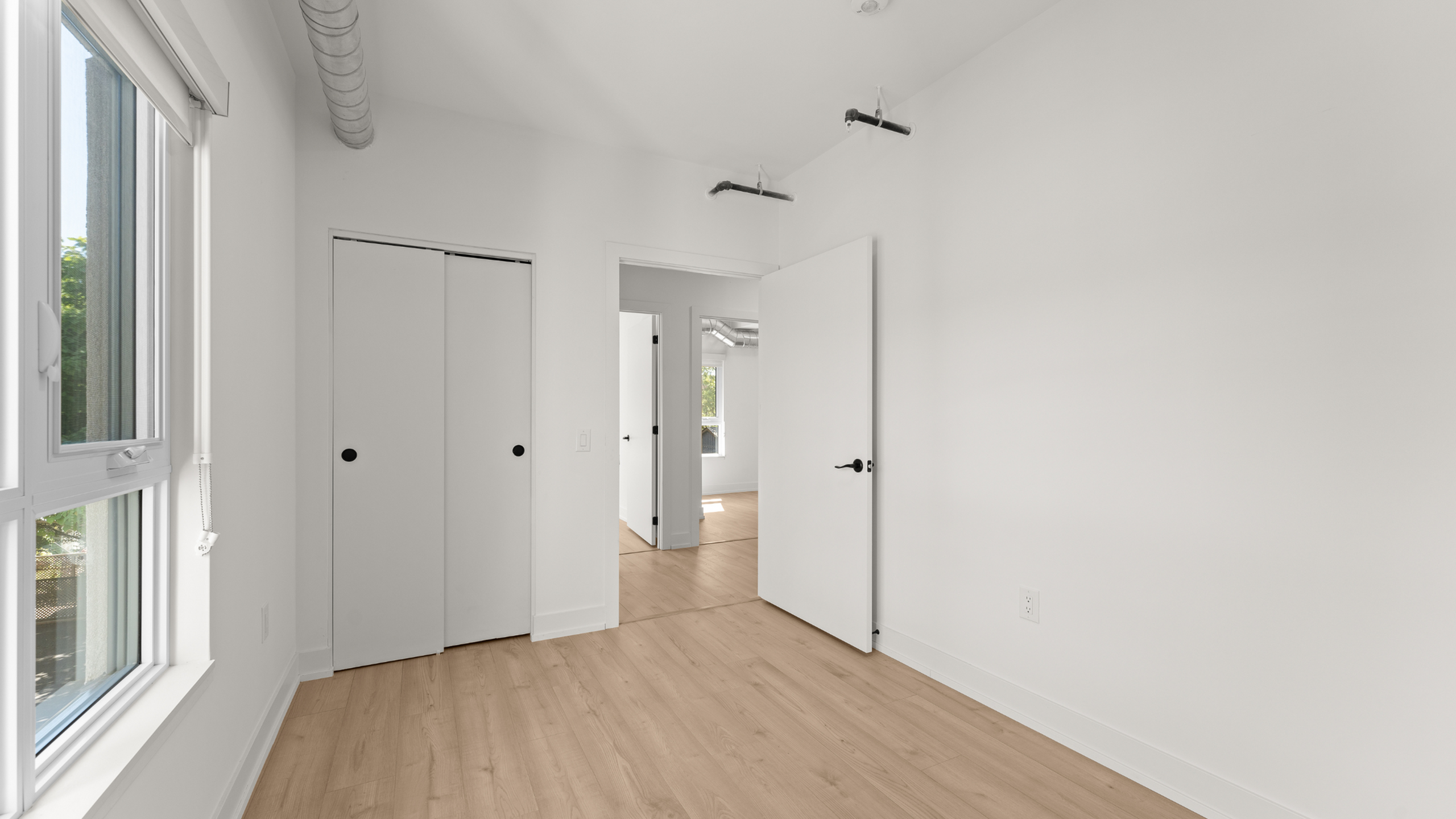 Bright modern room with large window, sleek closet doors, and stylish wood flooring showcasing minimalist design.