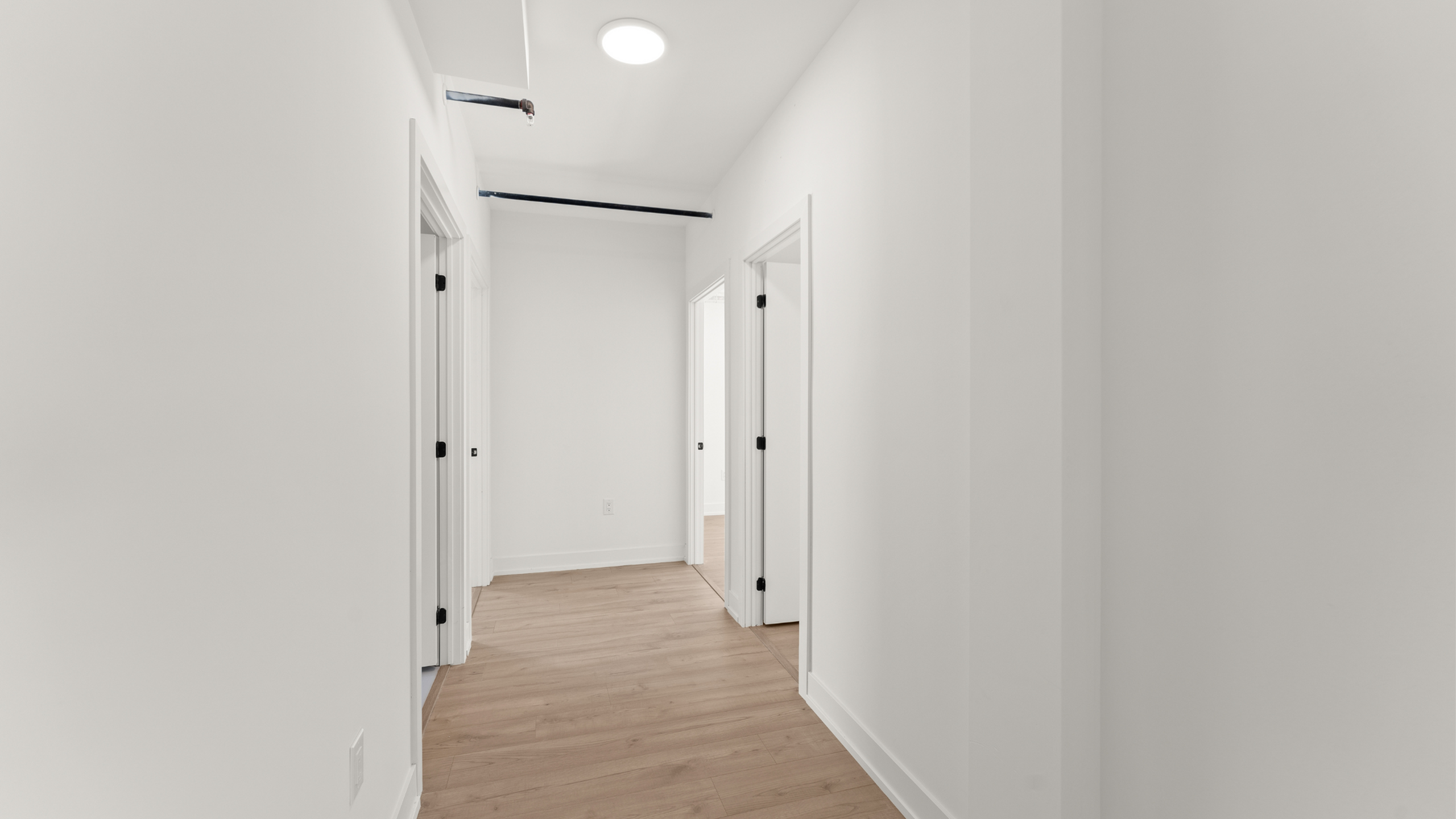 Bright and modern hallway with sleek white walls and elegant wooden flooring, leading to multiple rooms.