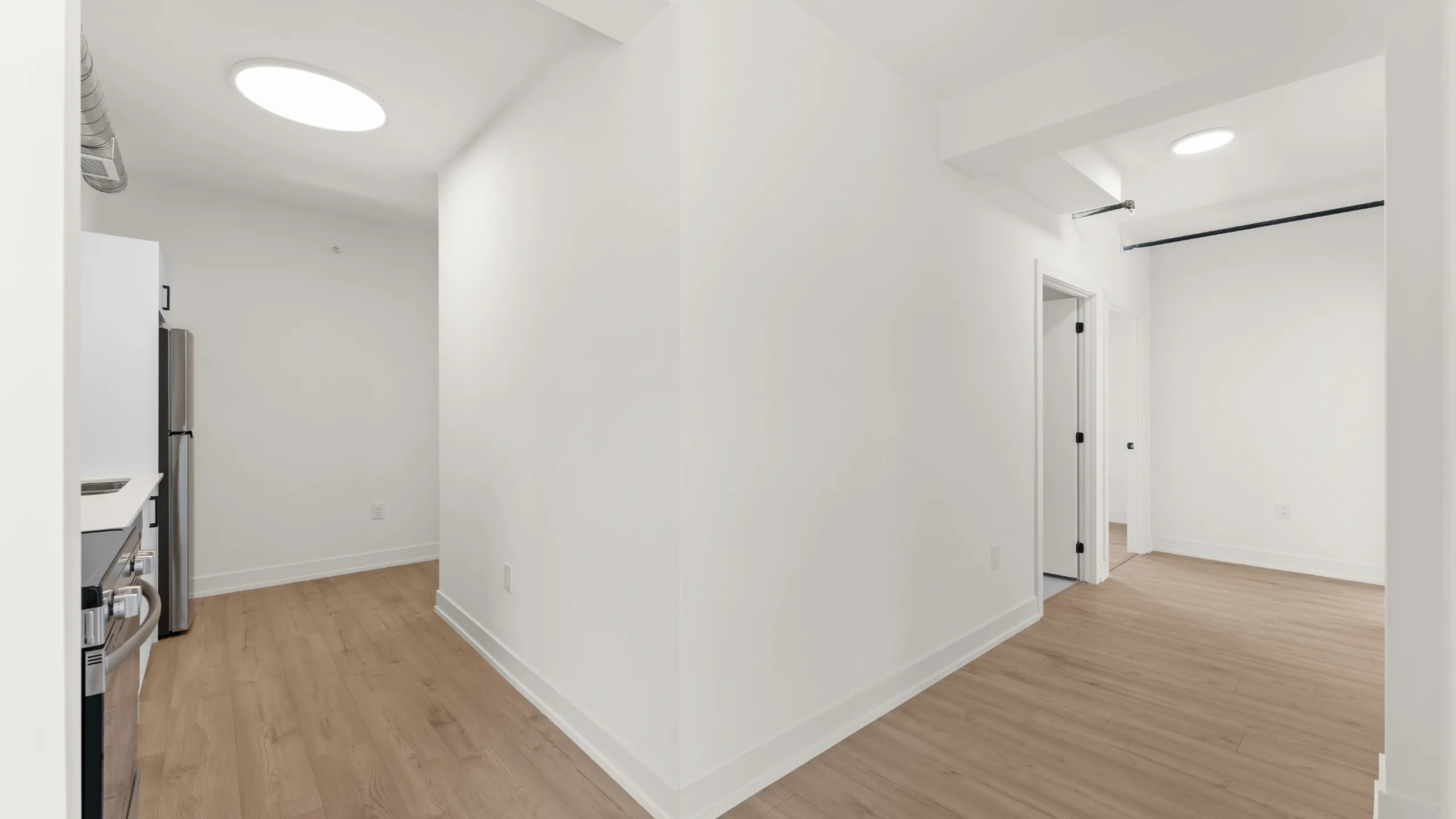Bright modern apartment hallway with sleek wood flooring and recessed lighting.