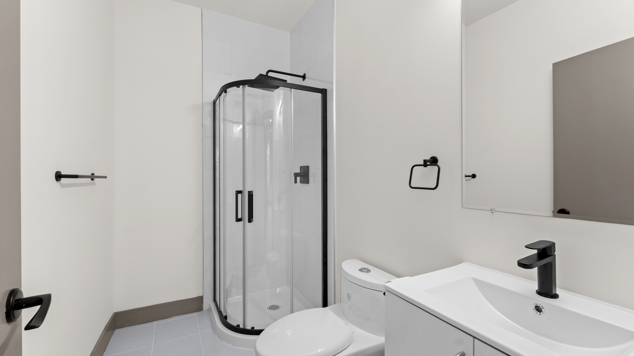 Elegant bathroom featuring a modern glass shower, a sleek white vanity, and minimalist black fixtures.