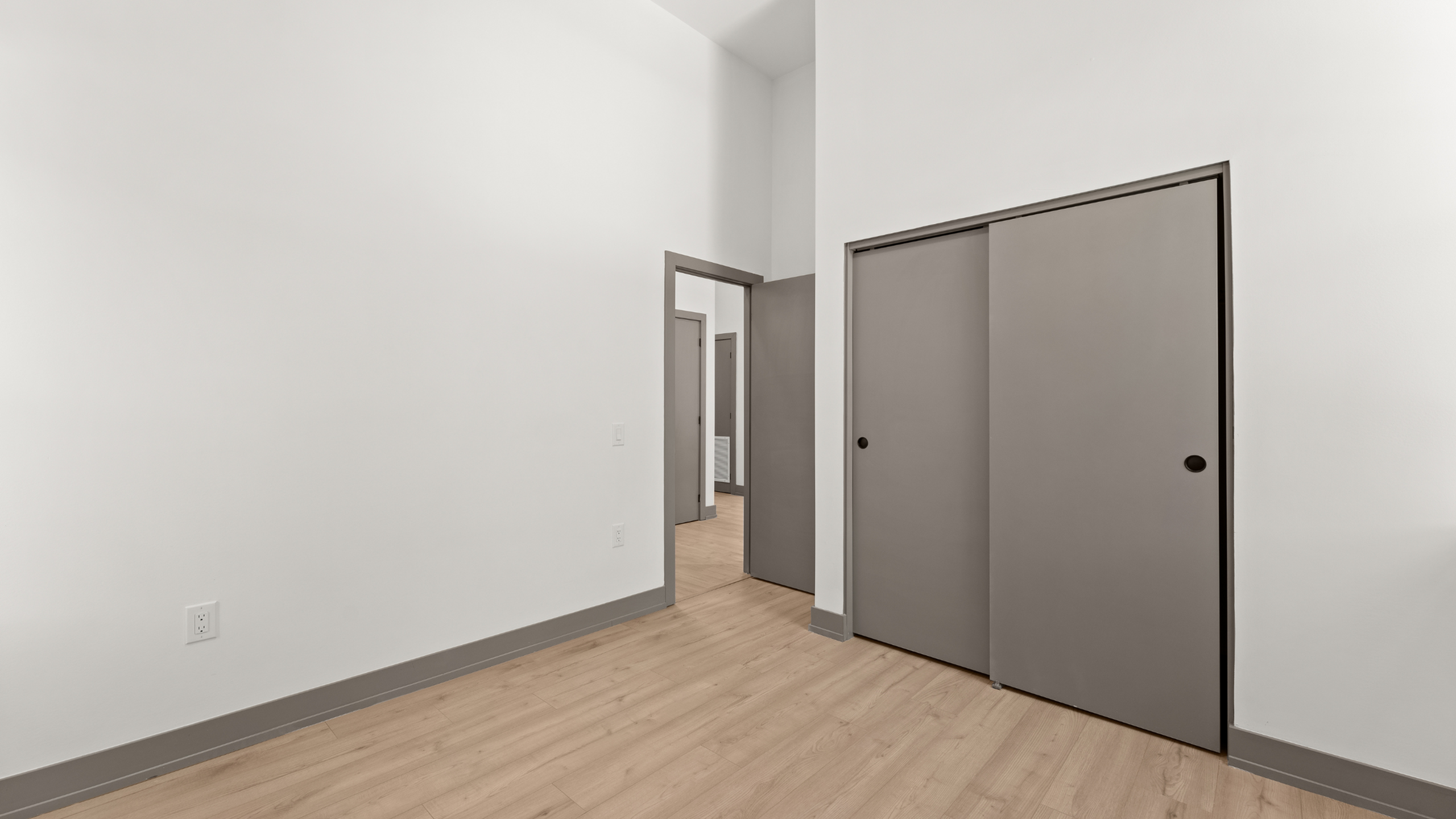 Bright and spacious room showcasing elegant wood flooring, tall white walls, and sleek sliding closet doors for a modern touch.