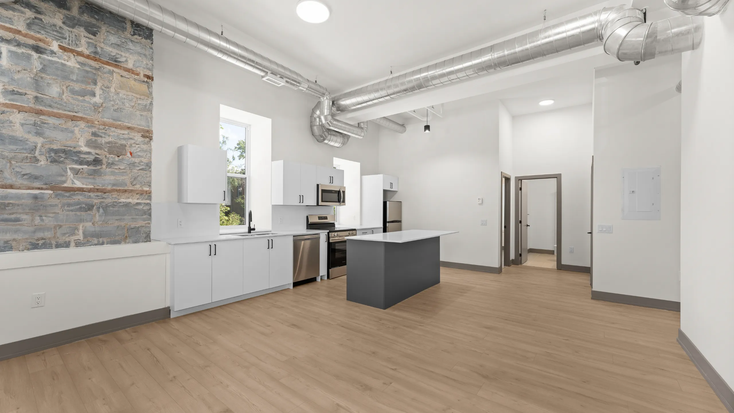 Modern open-concept kitchen featuring sleek white cabinetry, stainless steel appliances, and rustic exposed brick accent wall.