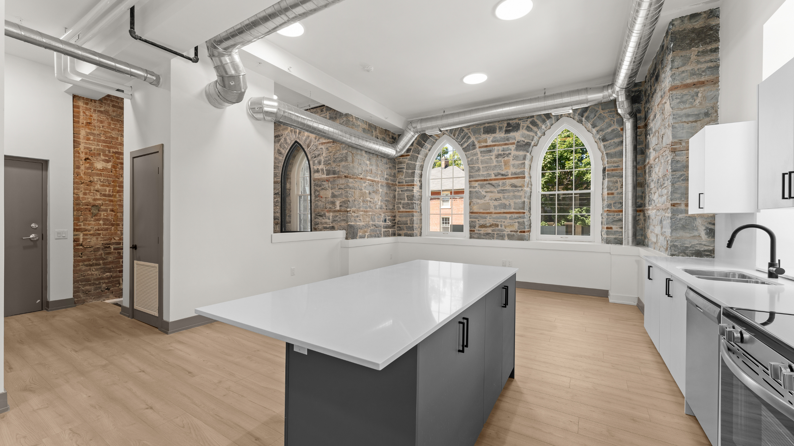 Chic modern kitchen with industrial exposed pipes, historic stone walls, and sleek appliances.