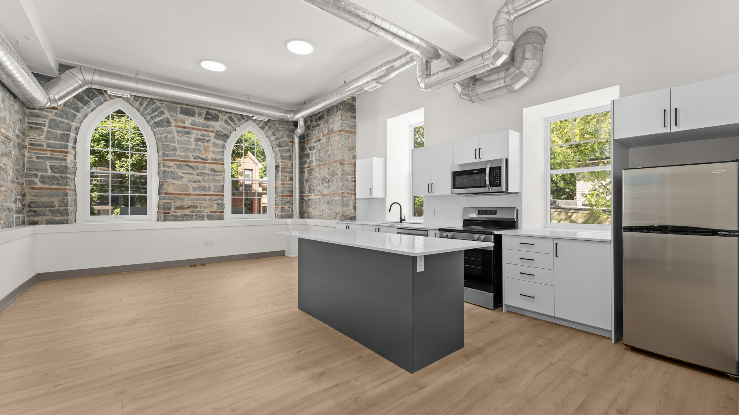 Bright modern kitchen with elegant stone walls, stainless steel appliances, large island, and stylish arched windows.