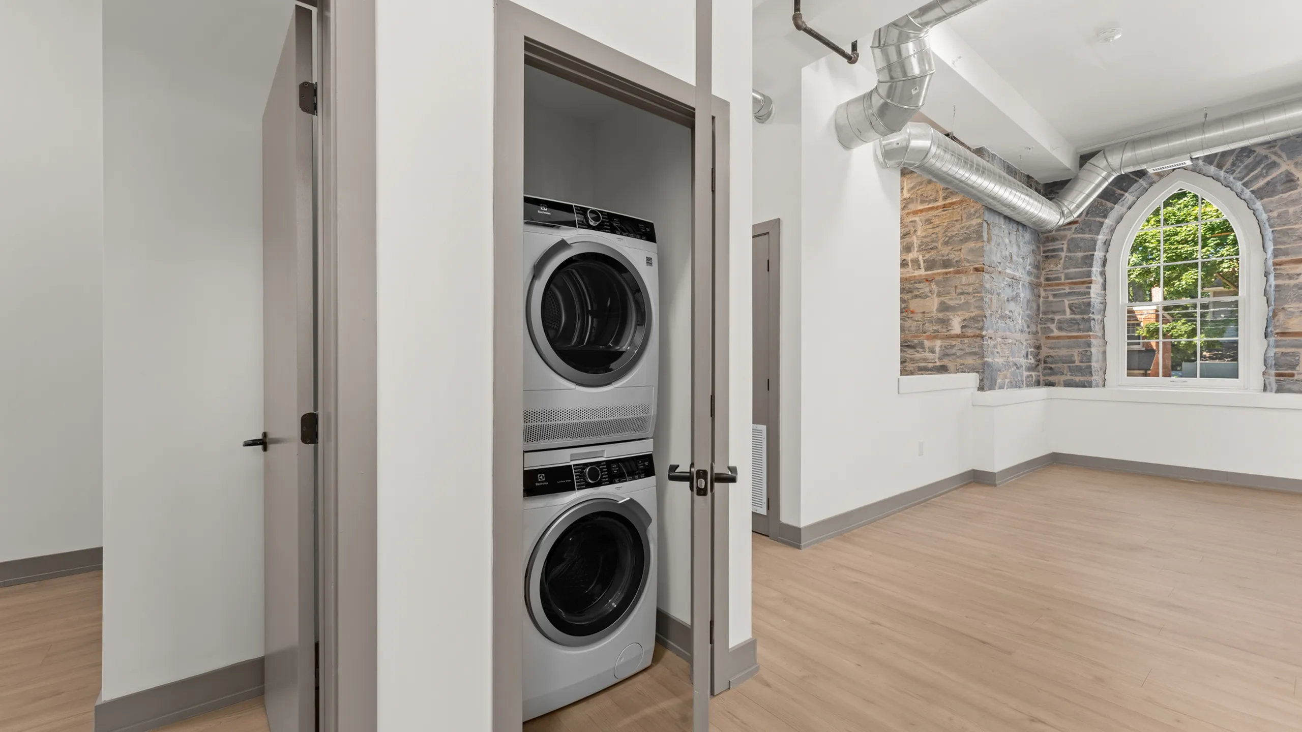Charming apartment featuring an in-unit stacked washer and dryer, with rustic stone wall accents and abundant natural light through a stylish arched window.