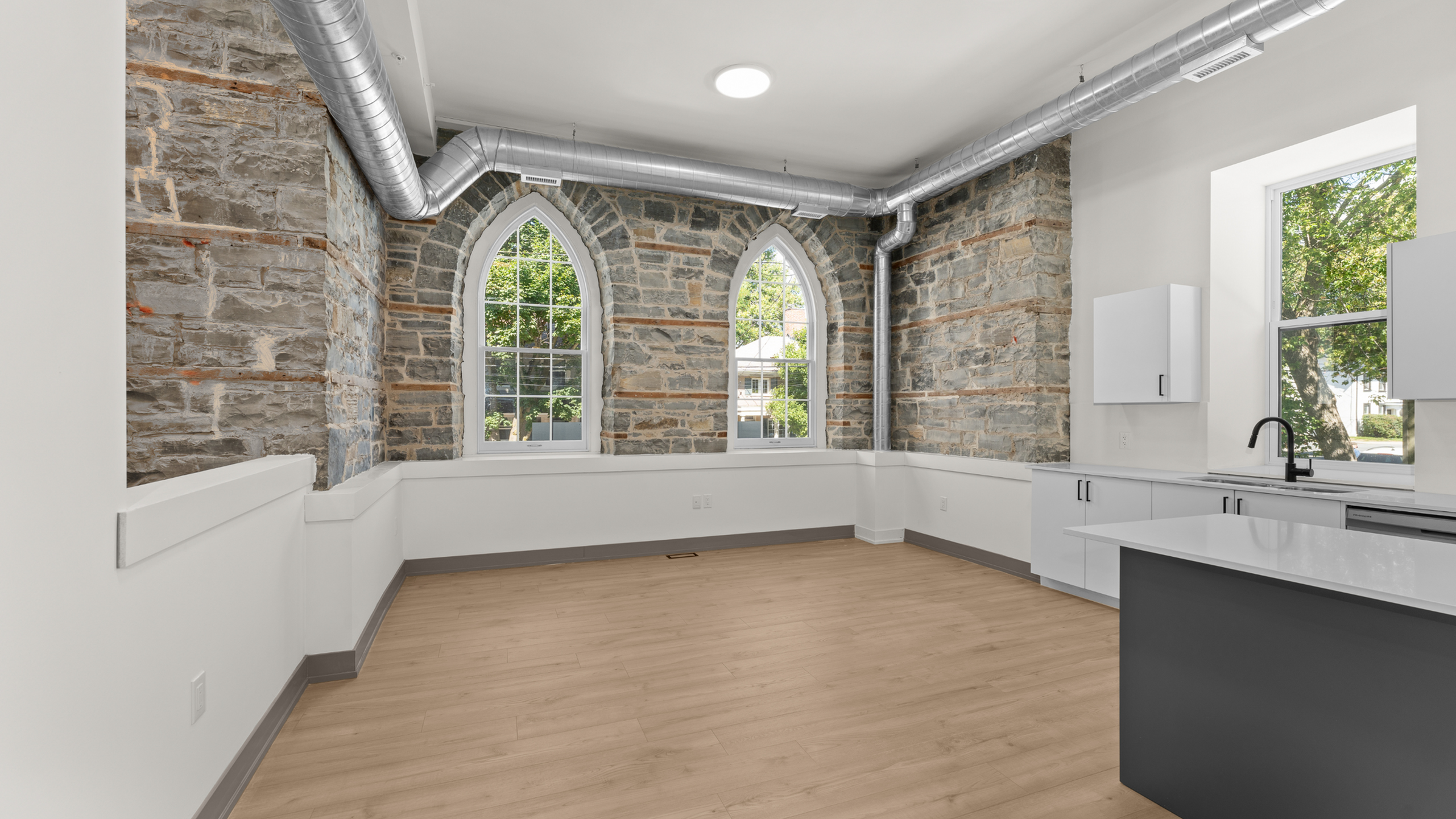 Chic apartment space featuring exposed stone walls, arched windows, and modern kitchen with sleek cabinetry and hardwood floors.