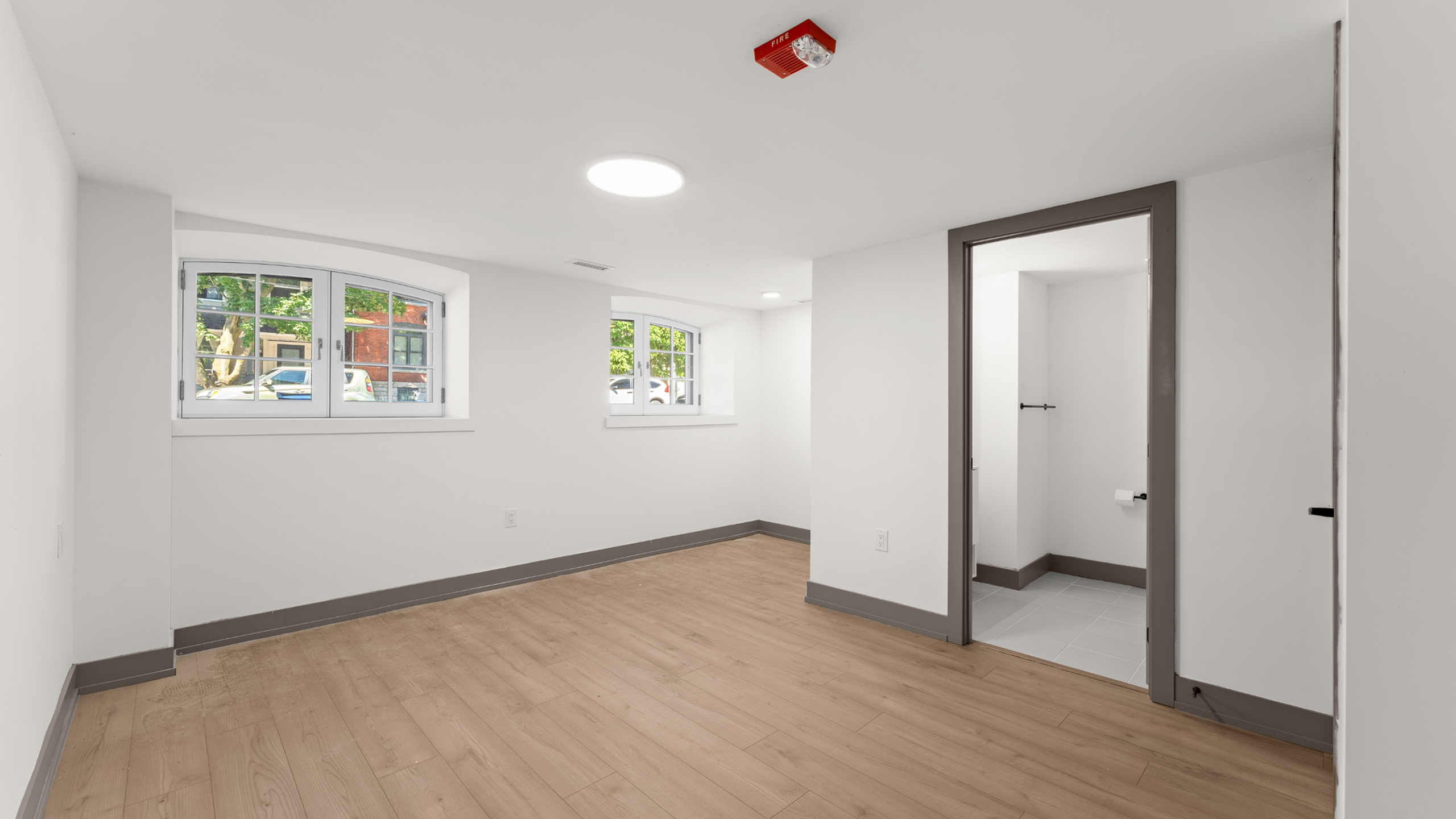 Bright basement room with large windows, modern recessed lighting, and wood-style flooring.