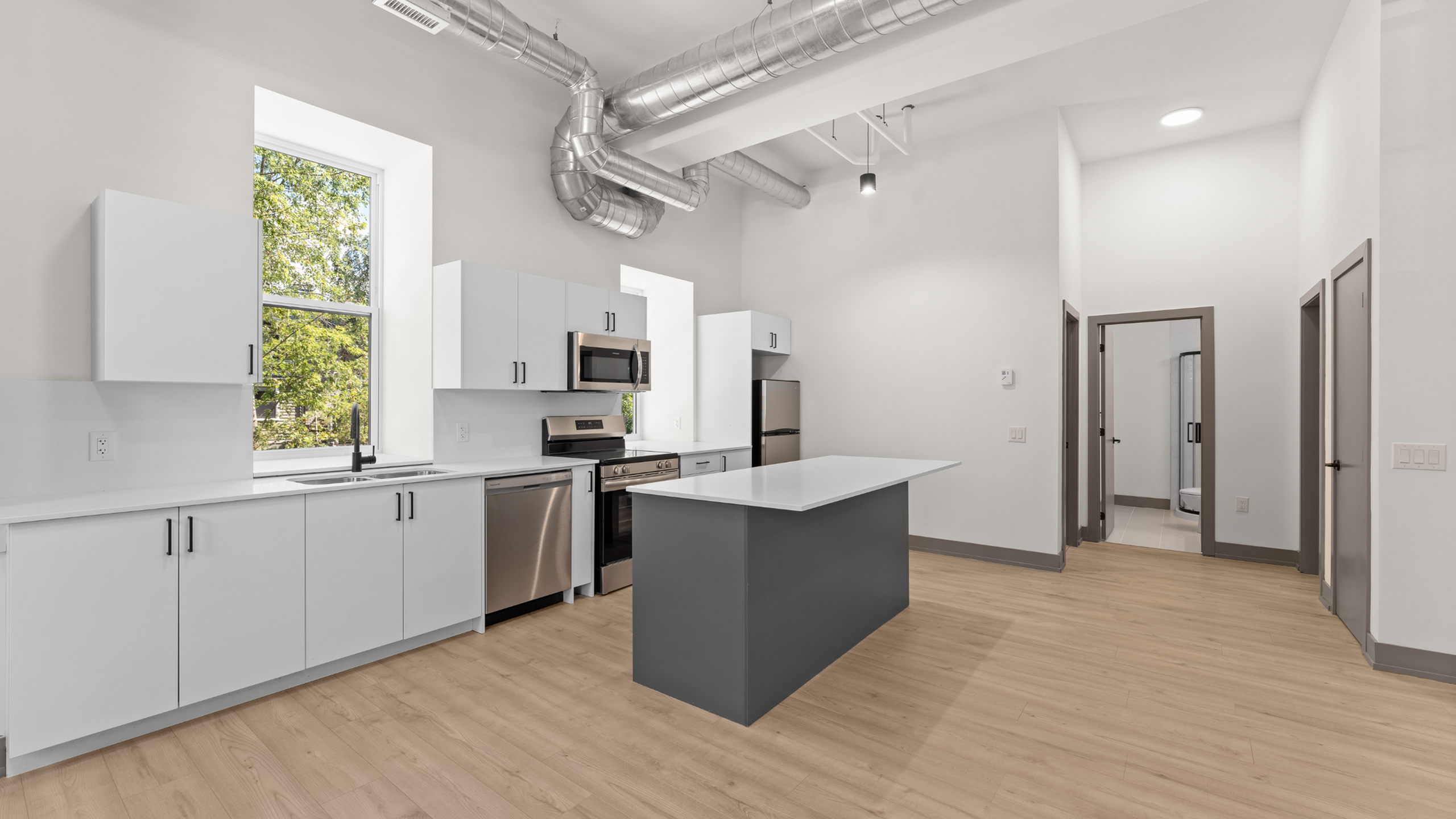 Modern open-concept kitchen with sleek white cabinetry, stainless steel appliances, and natural light streaming through a large window.