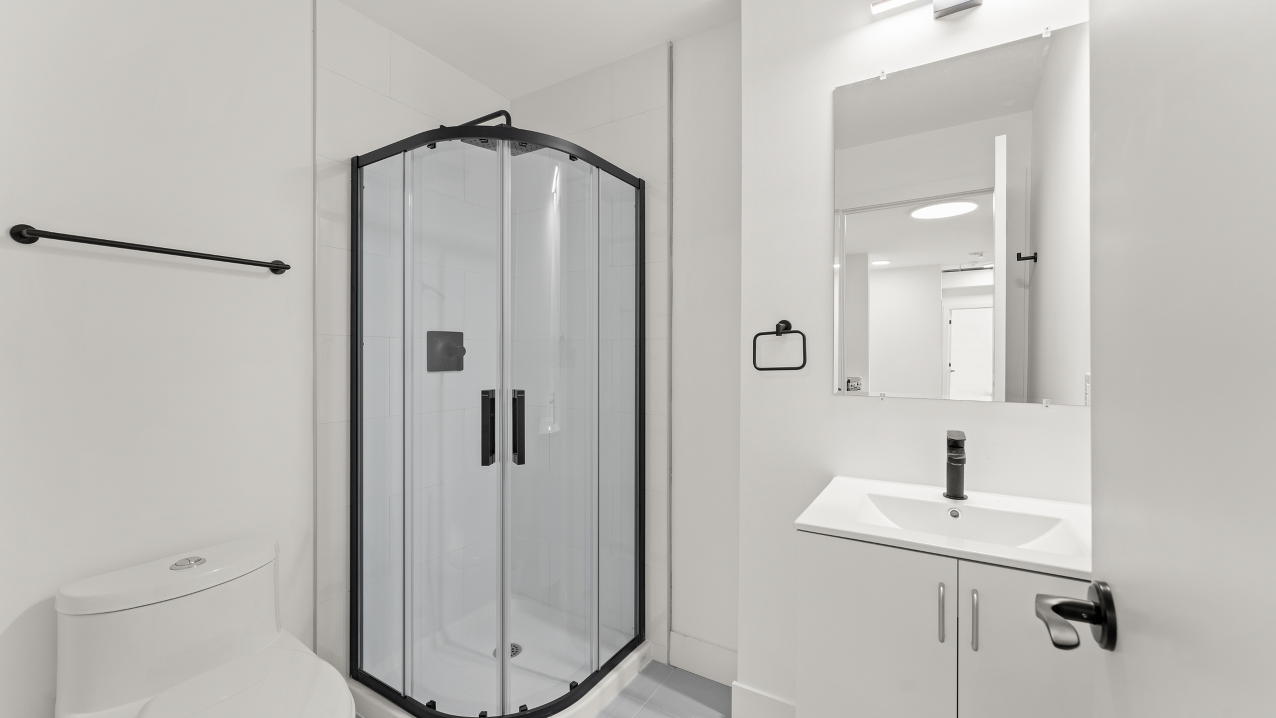 Modern bathroom featuring a sleek glass shower enclosure, white vanity with a chic faucet, and contemporary lighting.