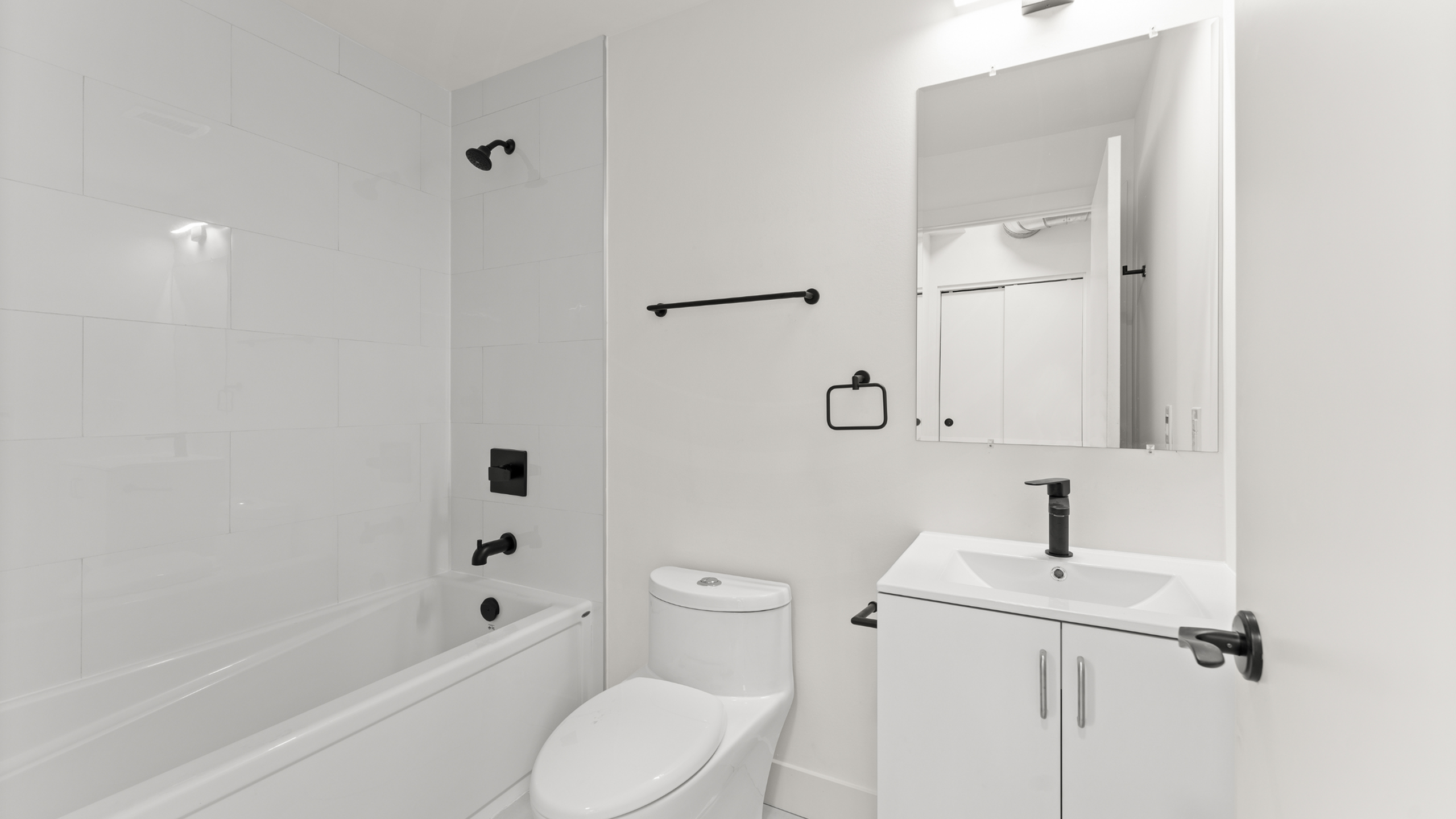 Elegant contemporary bathroom with sleek white tiles, modern fixtures, and a spacious vanity.