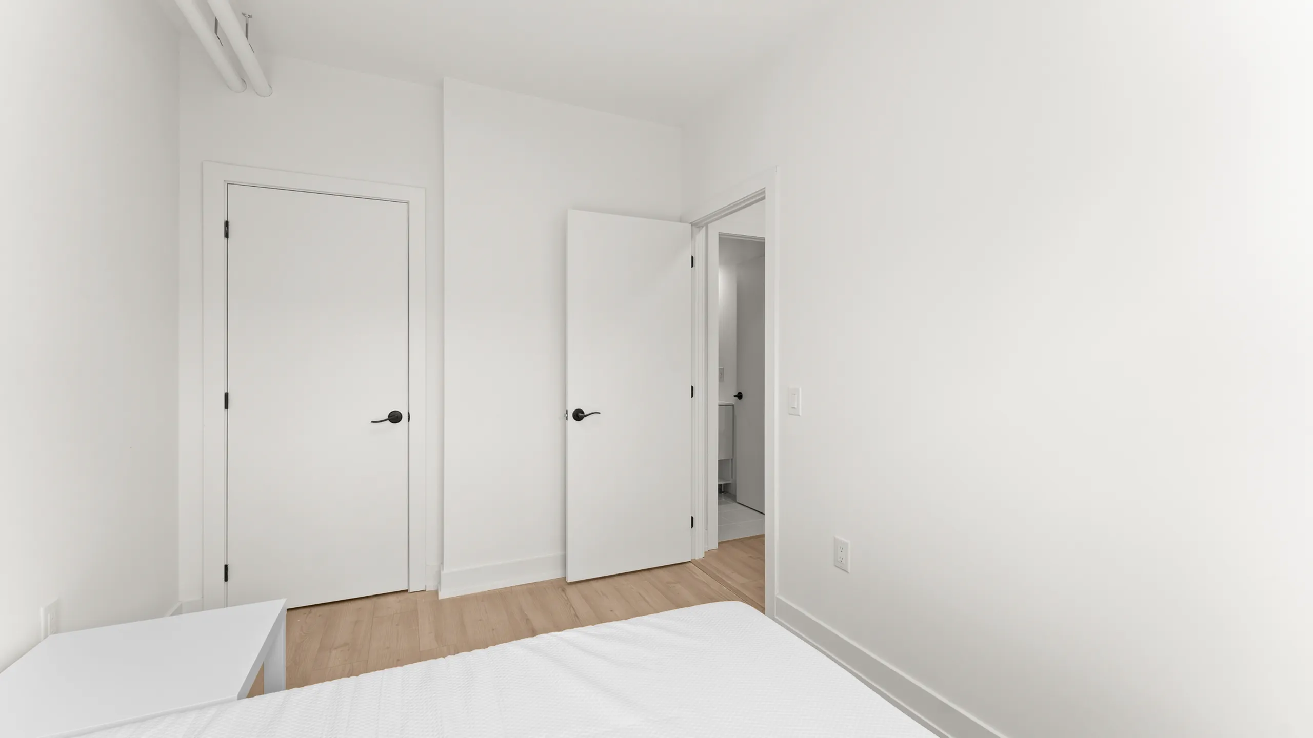 Minimalist bedroom with sleek white doors and light hardwood floors, emphasizing modern simplicity.