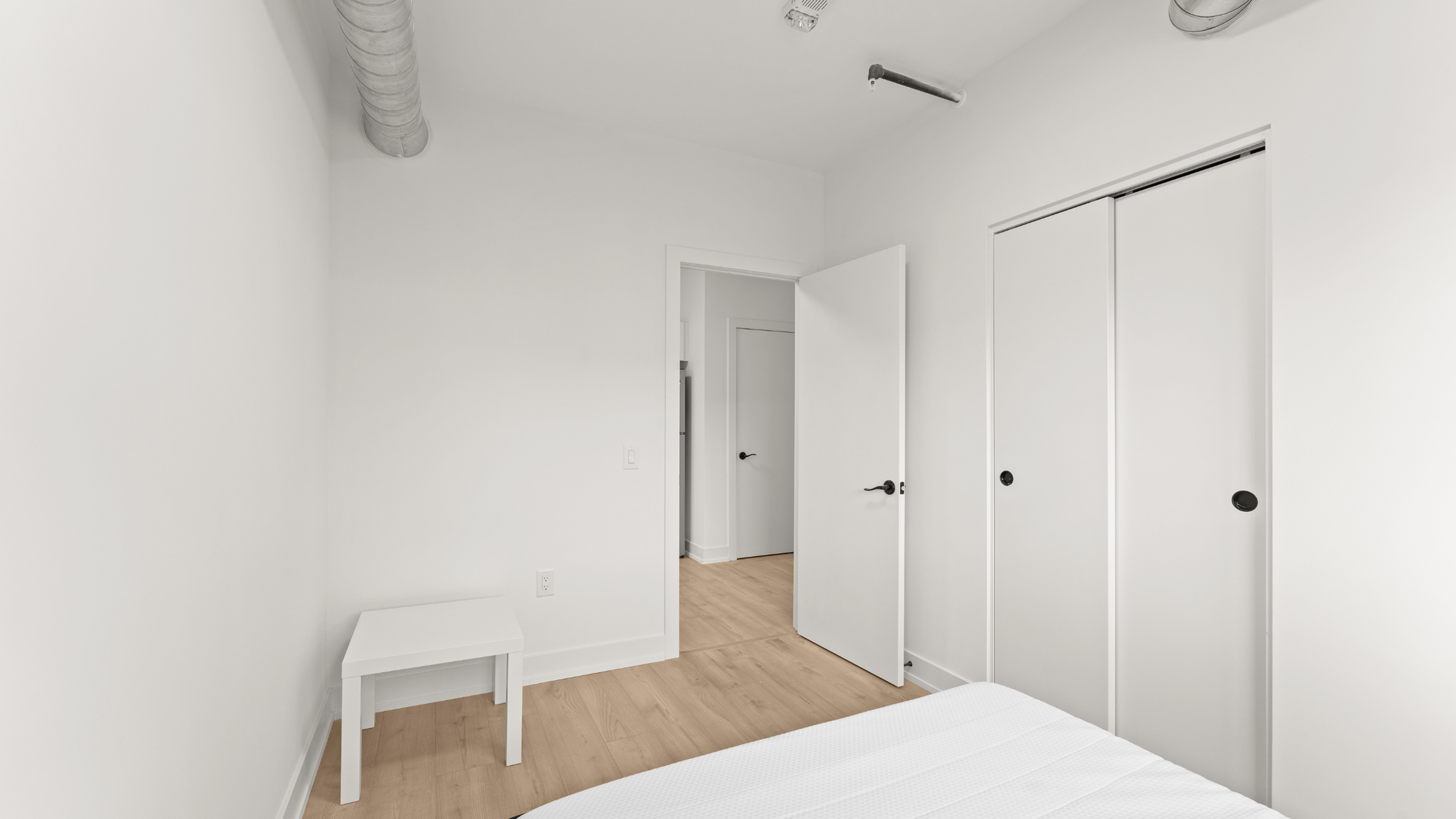 Bright and minimalist bedroom with white walls, wooden flooring, and spacious closet.