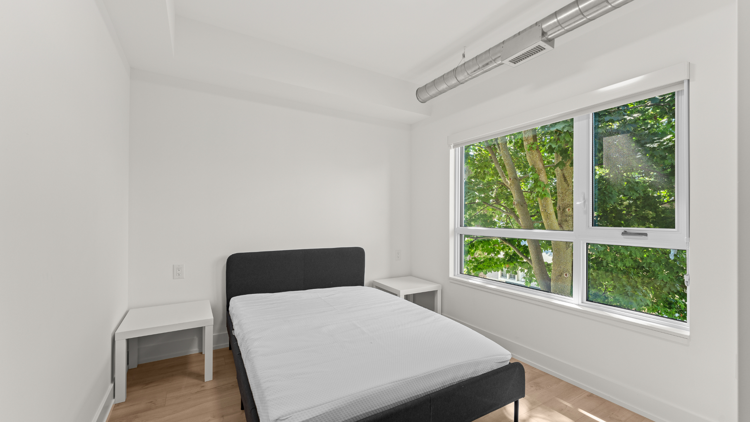 Bright and airy bedroom featuring a modern bed, minimalist white decor, and a large window with lush green views.