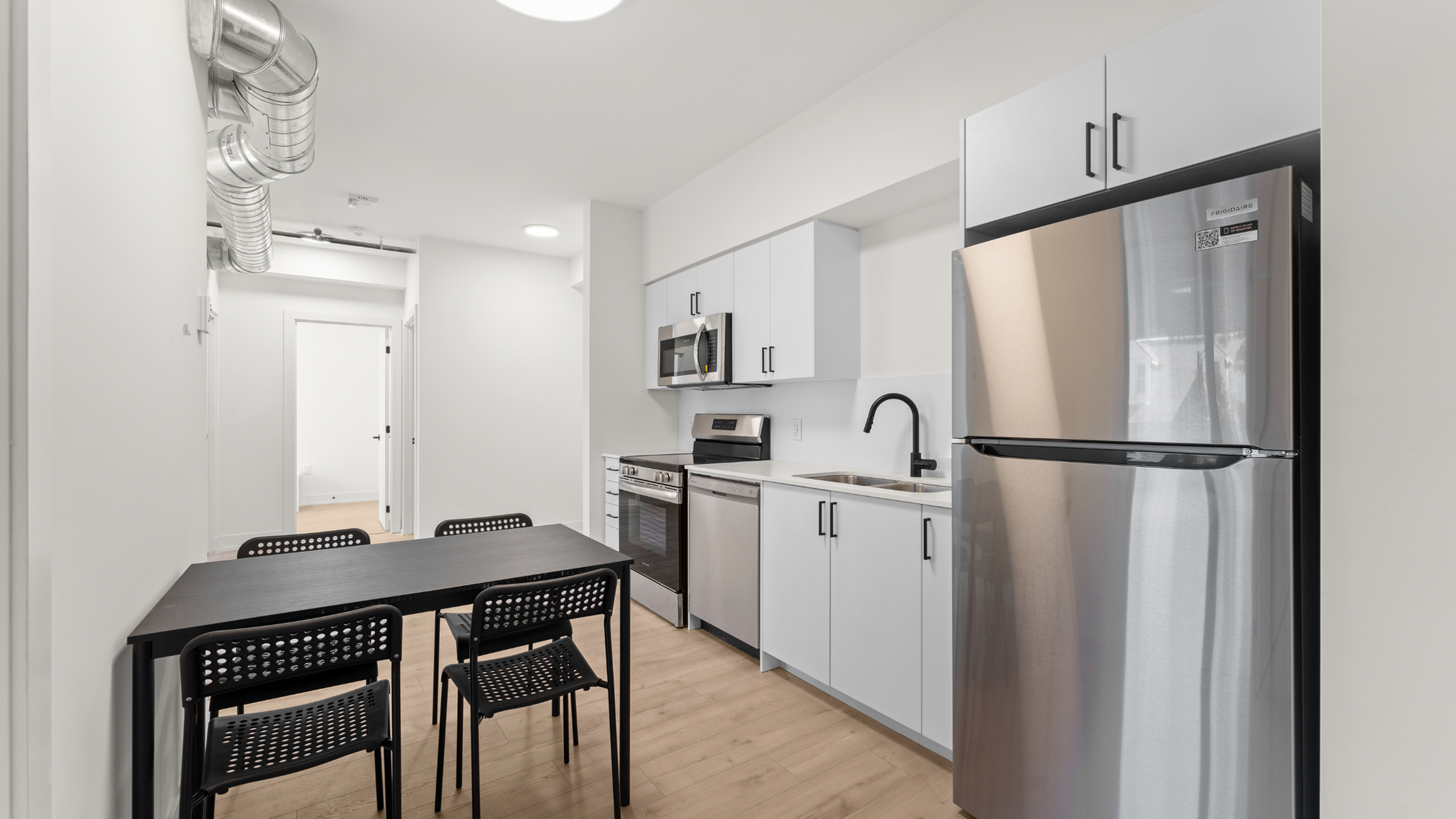 Modern kitchen area with sleek stainless steel appliances, stylish black dining table, and contemporary cabinetry.