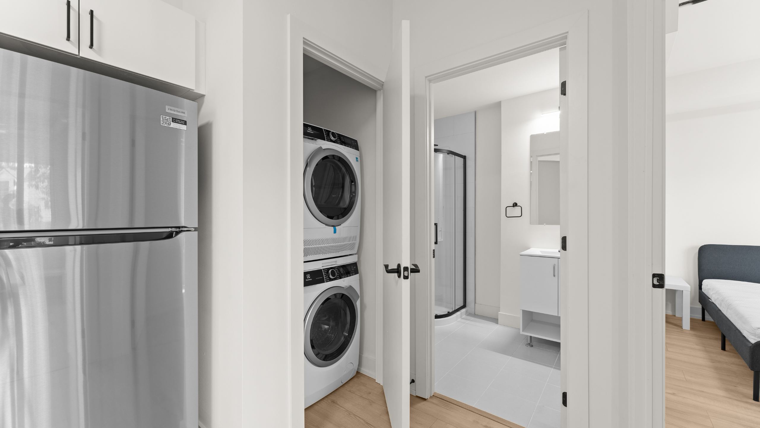 Modern apartment hallway featuring in-unit stacked washer and dryer, adjacent to a sleek bathroom with a spacious shower.