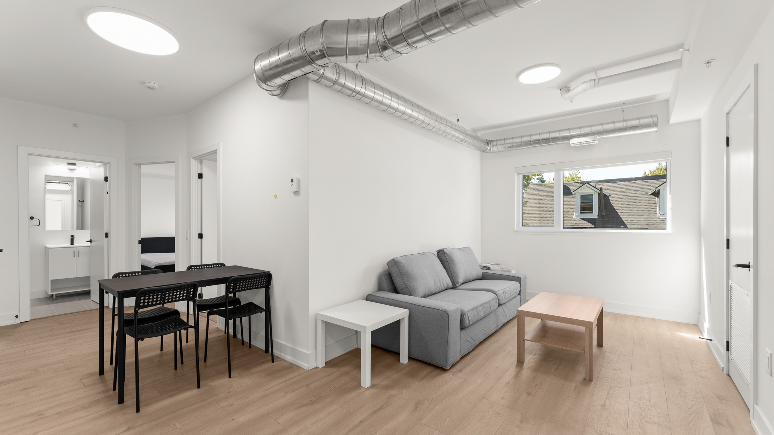 Bright and modern apartment featuring sleek open-plan design, cozy gray sofa, and elegant dining area with natural light from large window.
