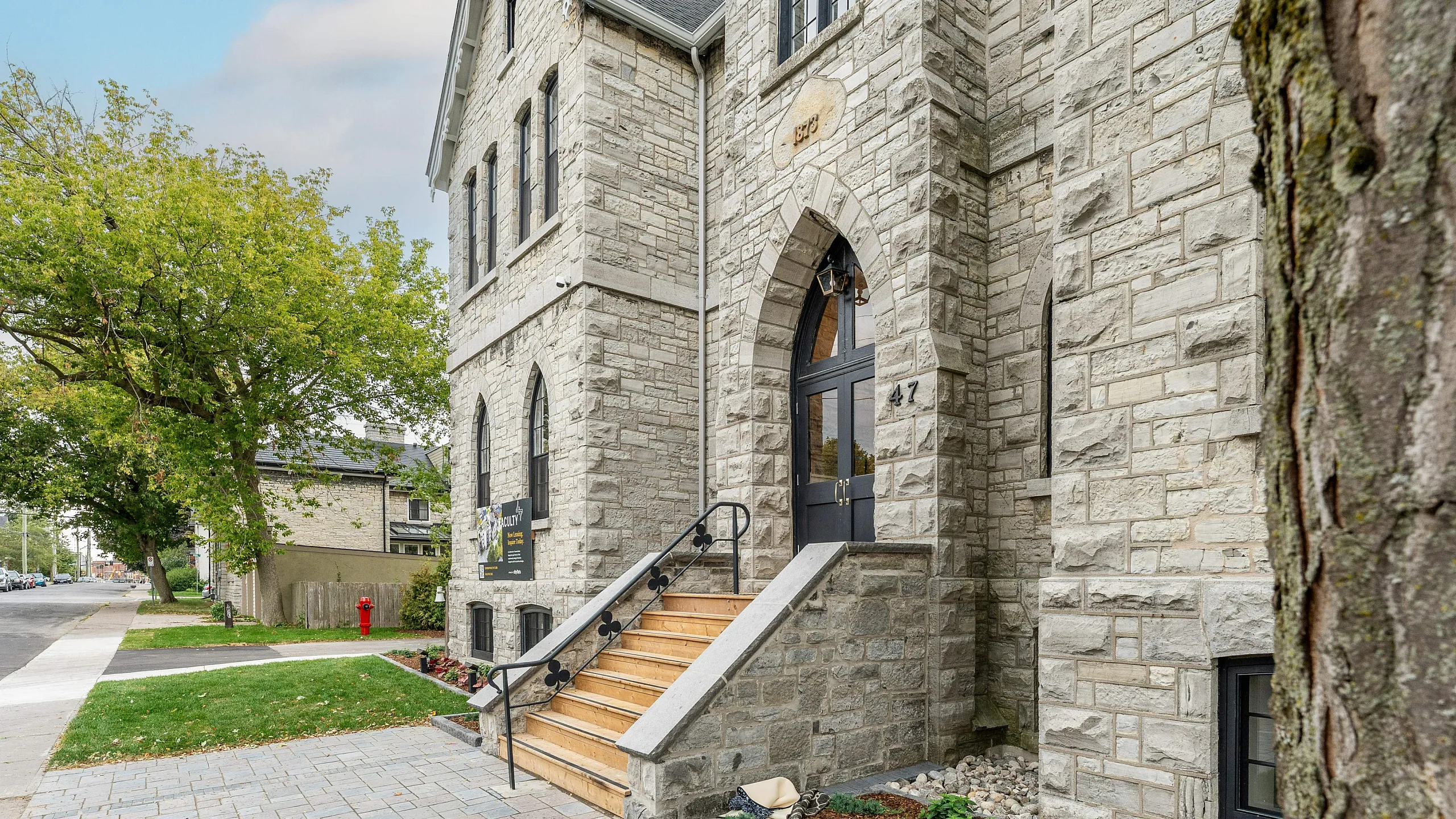 Charming stone building entrance with elegant wooden steps, nestled in a quaint neighborhood with lush trees and manicured landscaping.
