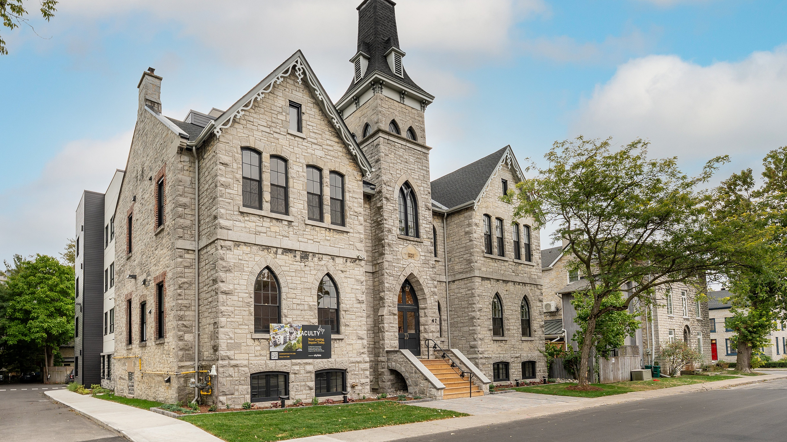 Charming historic stone building with modern extensions surrounded by lush greenery and a spacious driveway.