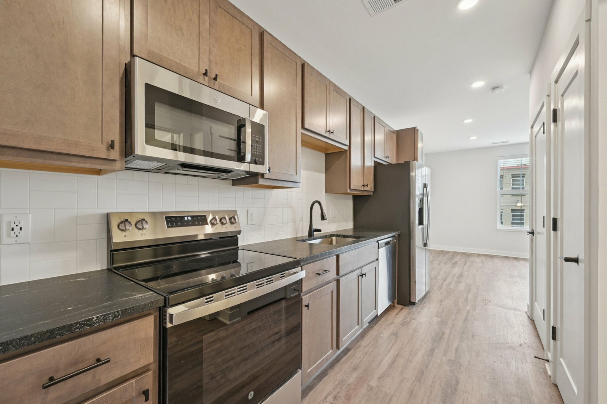 Modern kitchen with stainless steel appliances, sleek cabinetry, and a spacious layout featuring wood flooring and ample natural light.
