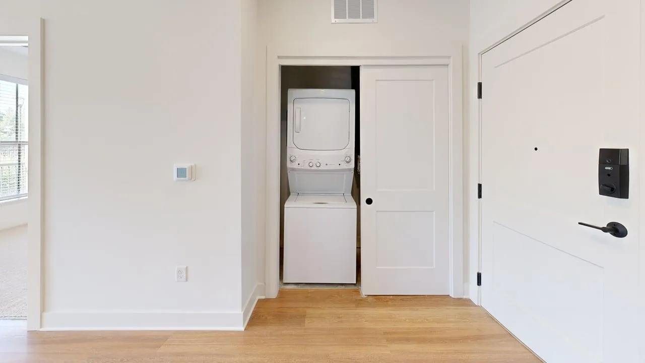 Modern apartment entryway featuring in-unit stacked washer and dryer with sleek sliding door and hardwood floors.