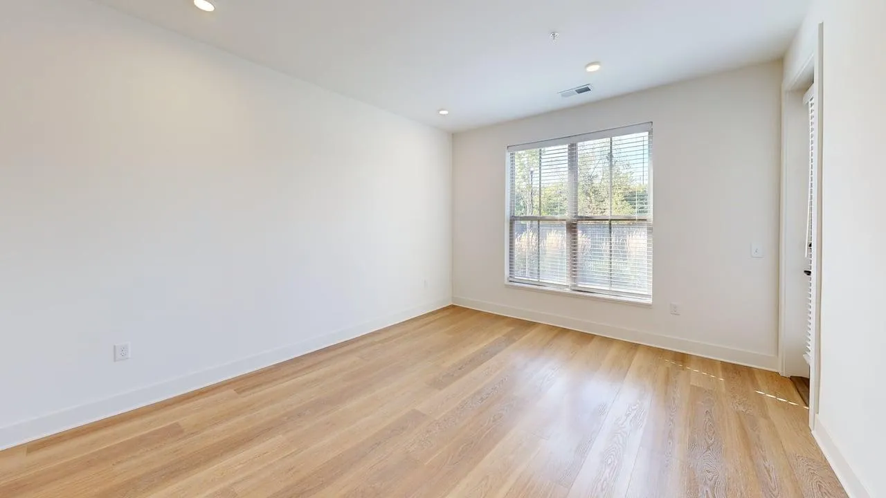 Bright and spacious empty room with large window and modern hardwood flooring, ready for personalization.