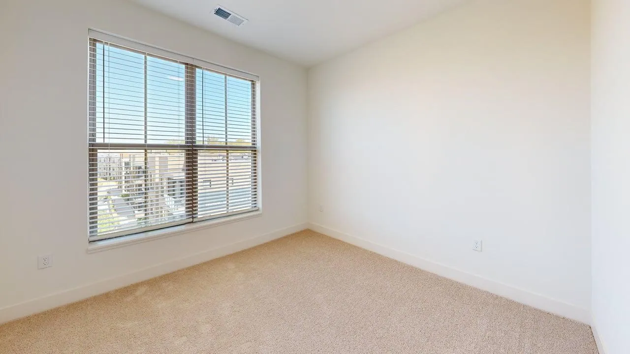 Bright and inviting room featuring large windows with blinds and soft carpet flooring, ideal for a cozy bedroom or home office.