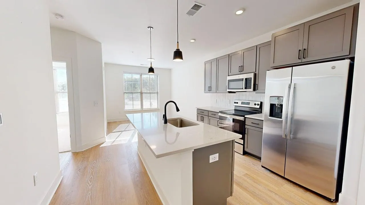 Modern kitchen space with sleek stainless steel appliances, stylish pendant lighting over a quartz island, and bright natural light from large windows.