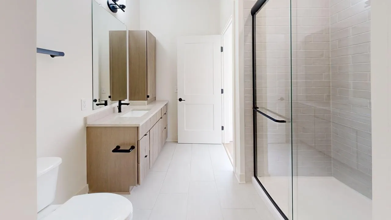 Elegant bathroom featuring modern glass shower, dual sinks with wooden cabinetry, and sleek tile flooring.