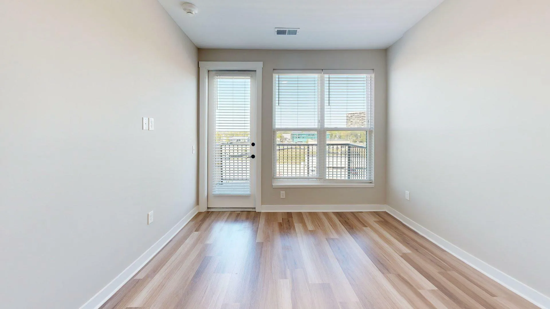 Bright and airy room with elegant wood flooring, large windows, and a door leading to a cozy balcony, perfect for urban living.