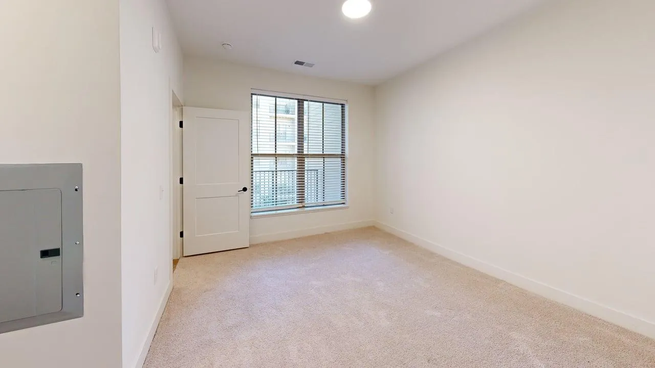 Bright, spacious bedroom with cozy carpeted floors, a large window for natural light, and a modern door design.