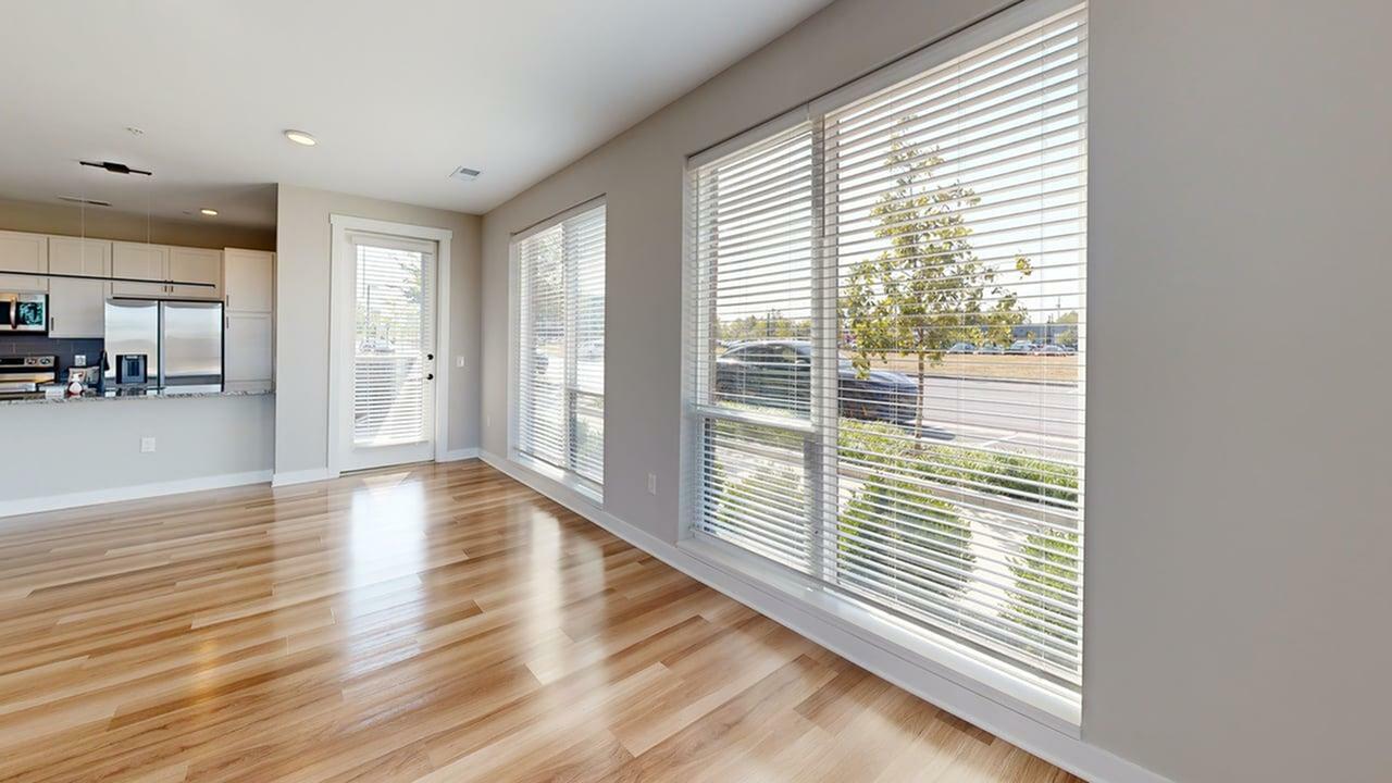 Bright, open-concept living room with large windows, sleek hardwood floors, and modern kitchen in the background.
