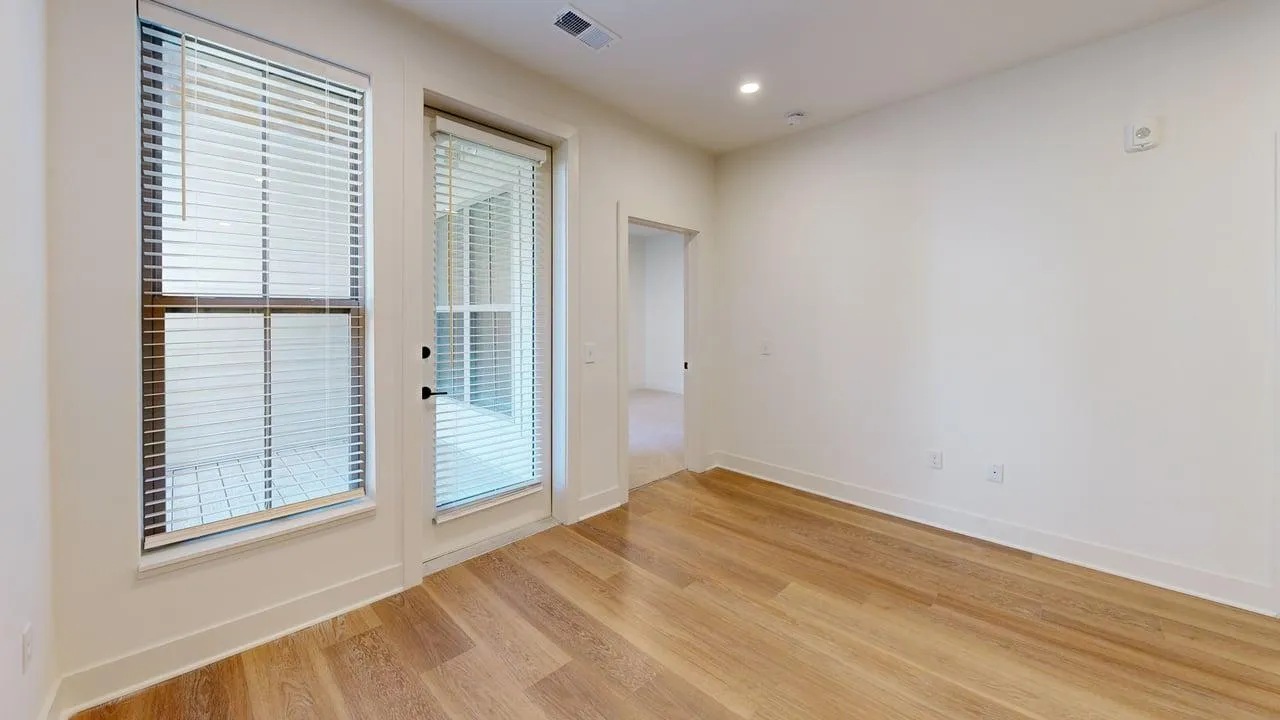 Bright and airy room with elegant wooden flooring, large windows, and a stylish glass door leading to additional space, perfect for a contemporary living area.