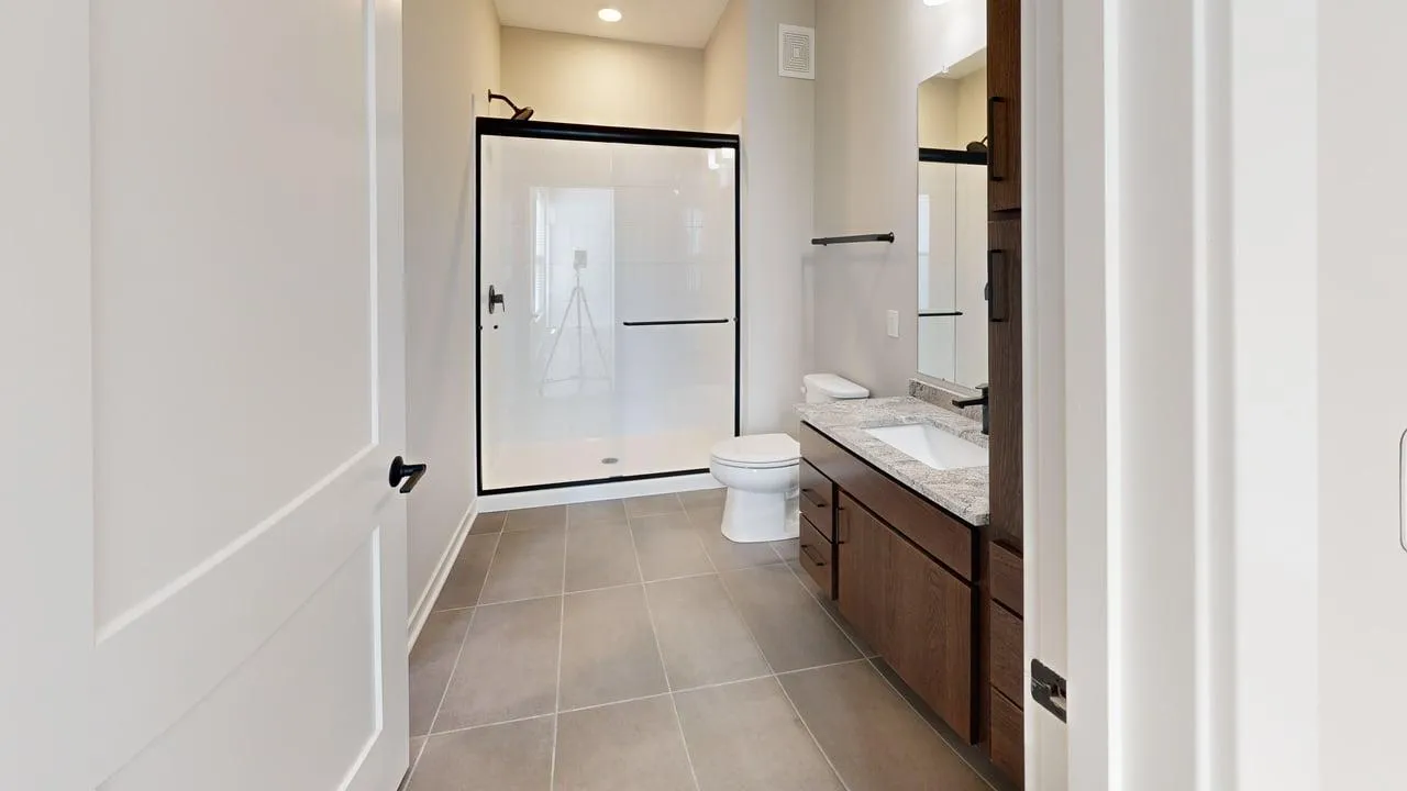 Modern bathroom featuring a large walk-in shower, elegant vanity with granite countertop, and sleek tile flooring.